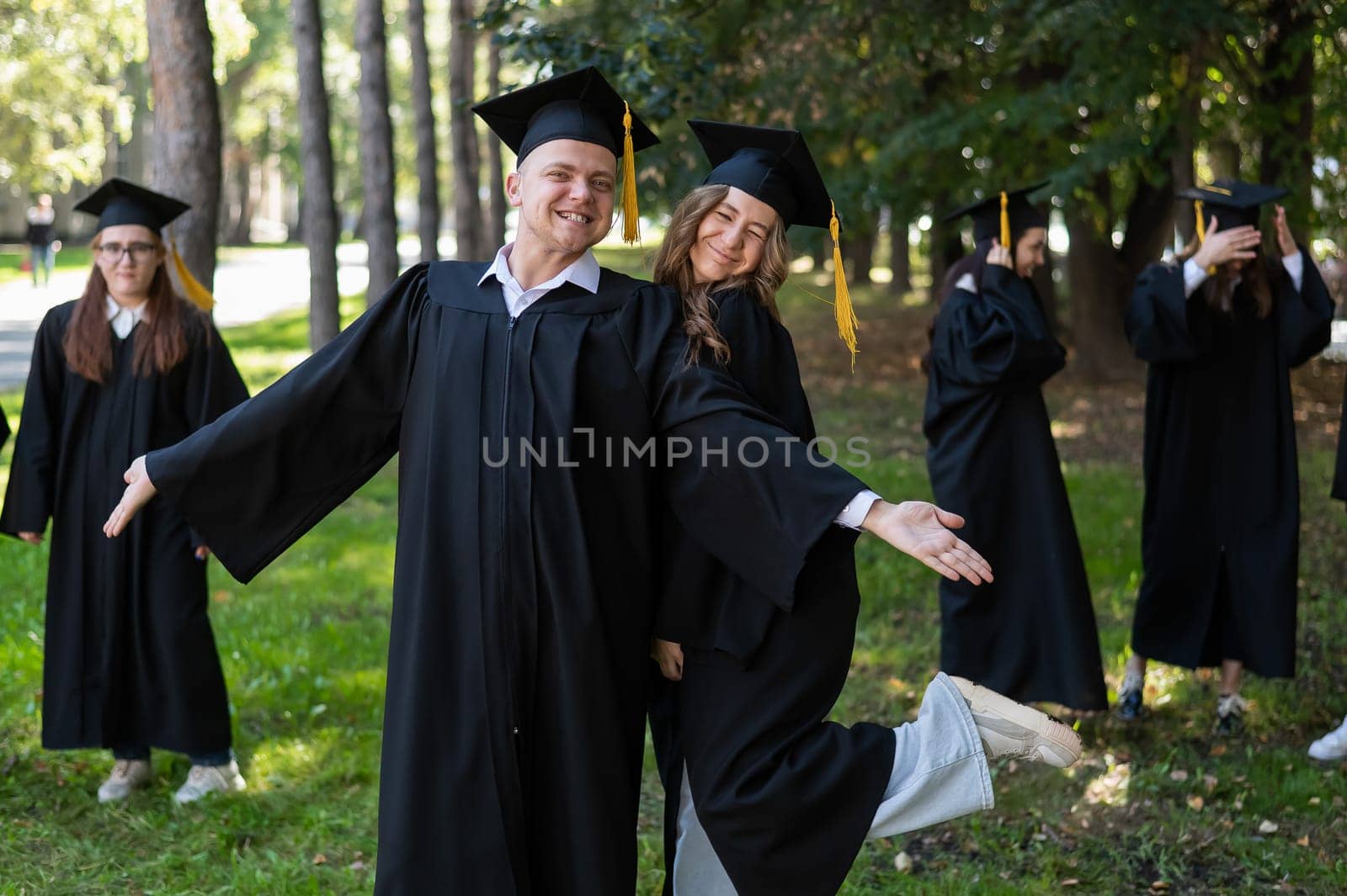 Group of happy young people in graduation gowns outdoors. Students are walking in the park. by mrwed54