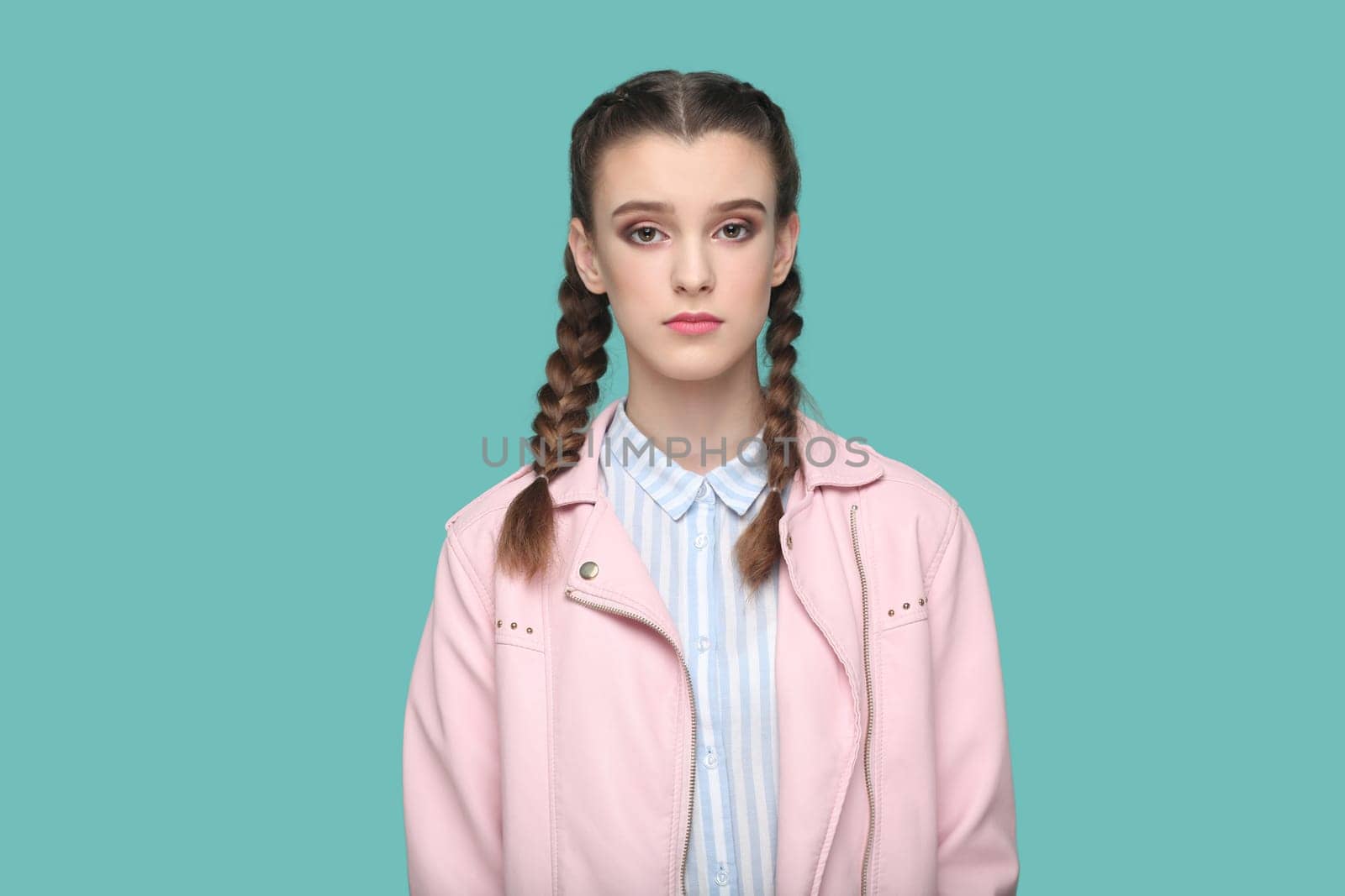 Serious strict teenager girl with braids wearing pink jacket looking at camera with bossy expression by Khosro1