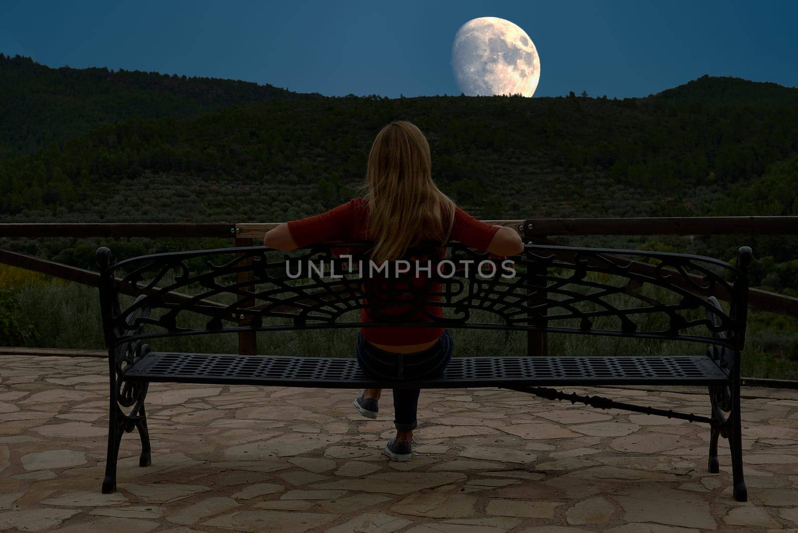 Blonde girl sitting on a bench with her back facing the moon.unrecognisable, caucasian, straight hair, red, forest, lonely, forge, maderam pines, relaxation , contemplation