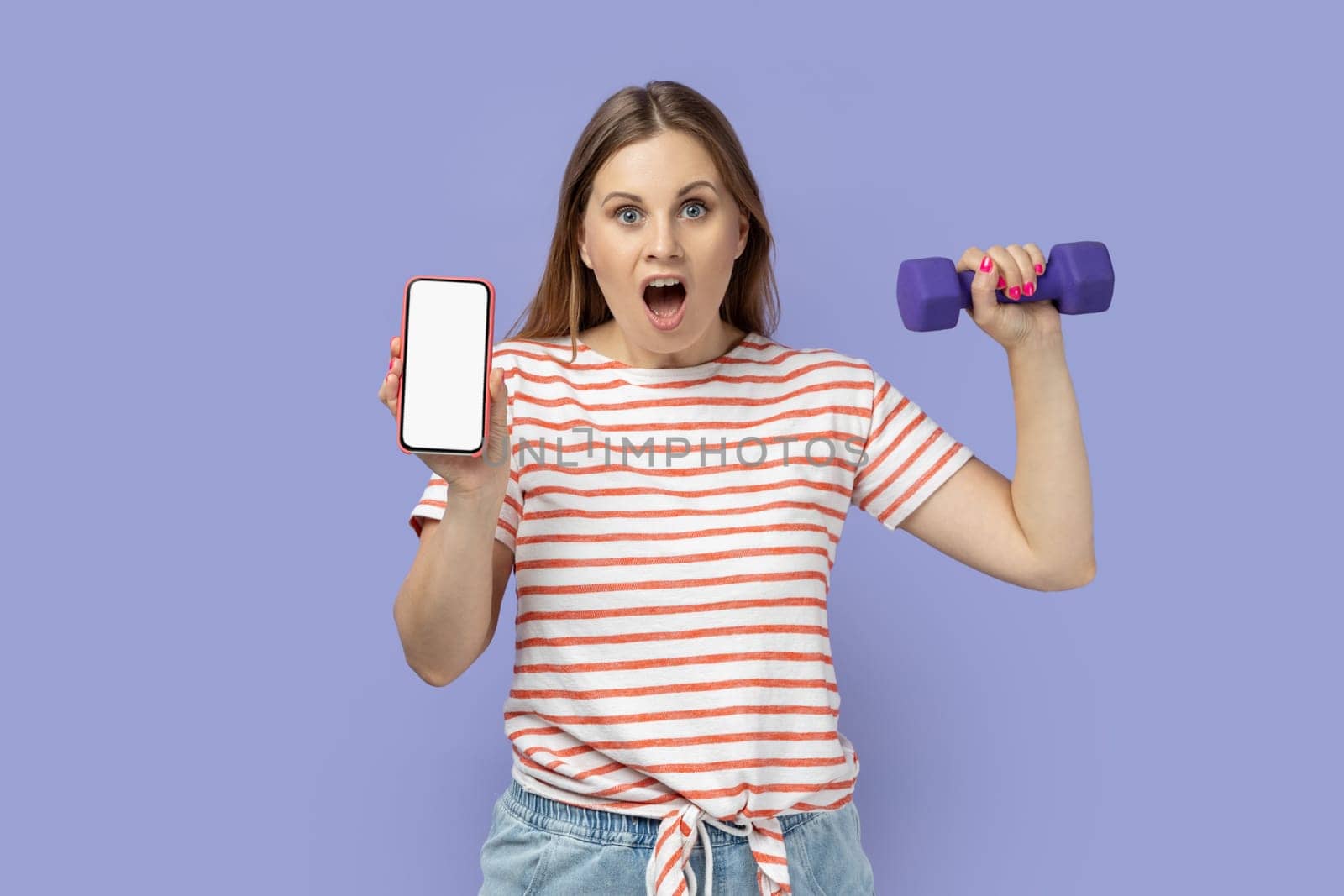 Woman holding dumbbell in hand and mobile phone with blank screen, space for advertisement. by Khosro1