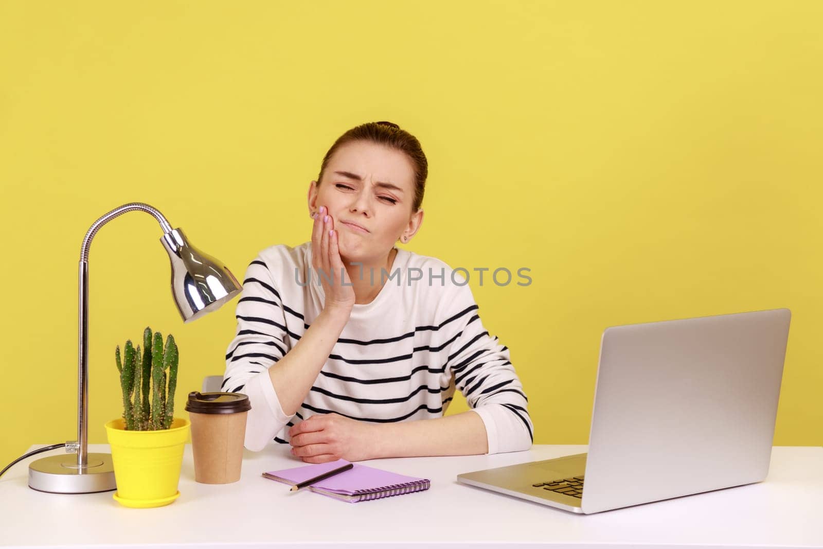 Unhealthy dissatisfied woman manager touching cheek feeling pain and discomfort in oral cavity, toothache and gums inflammation. Indoor studio studio shot isolated on yellow background.