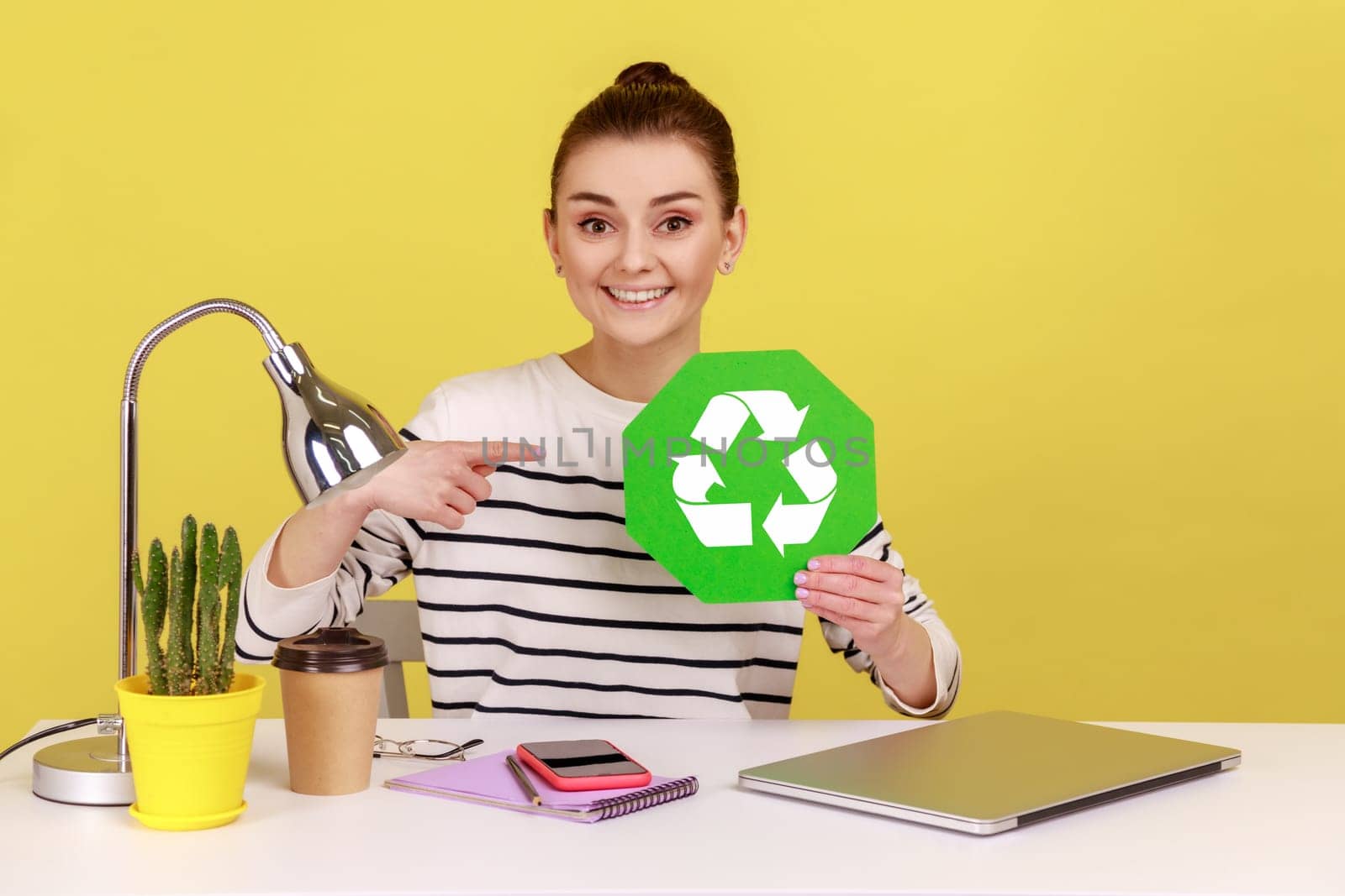 Woman pointing at green recycling symbol in hands, ecology concept, sitting on workplace with laptop by Khosro1