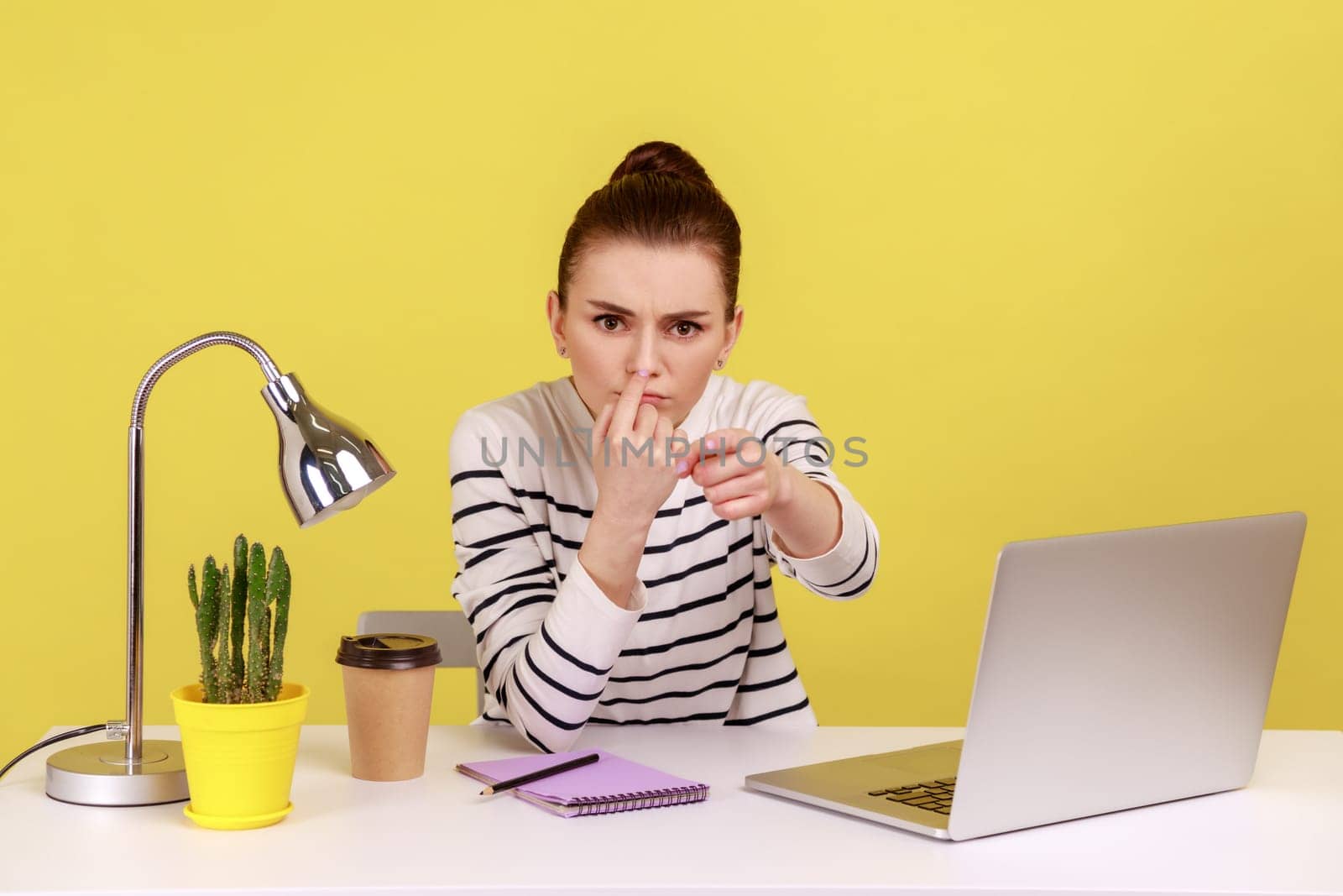 Portrait of bossy serious annoyed woman office manager touching nose, doing liar gesture, looking with suspicion at camera. Indoor studio studio shot isolated on yellow background.