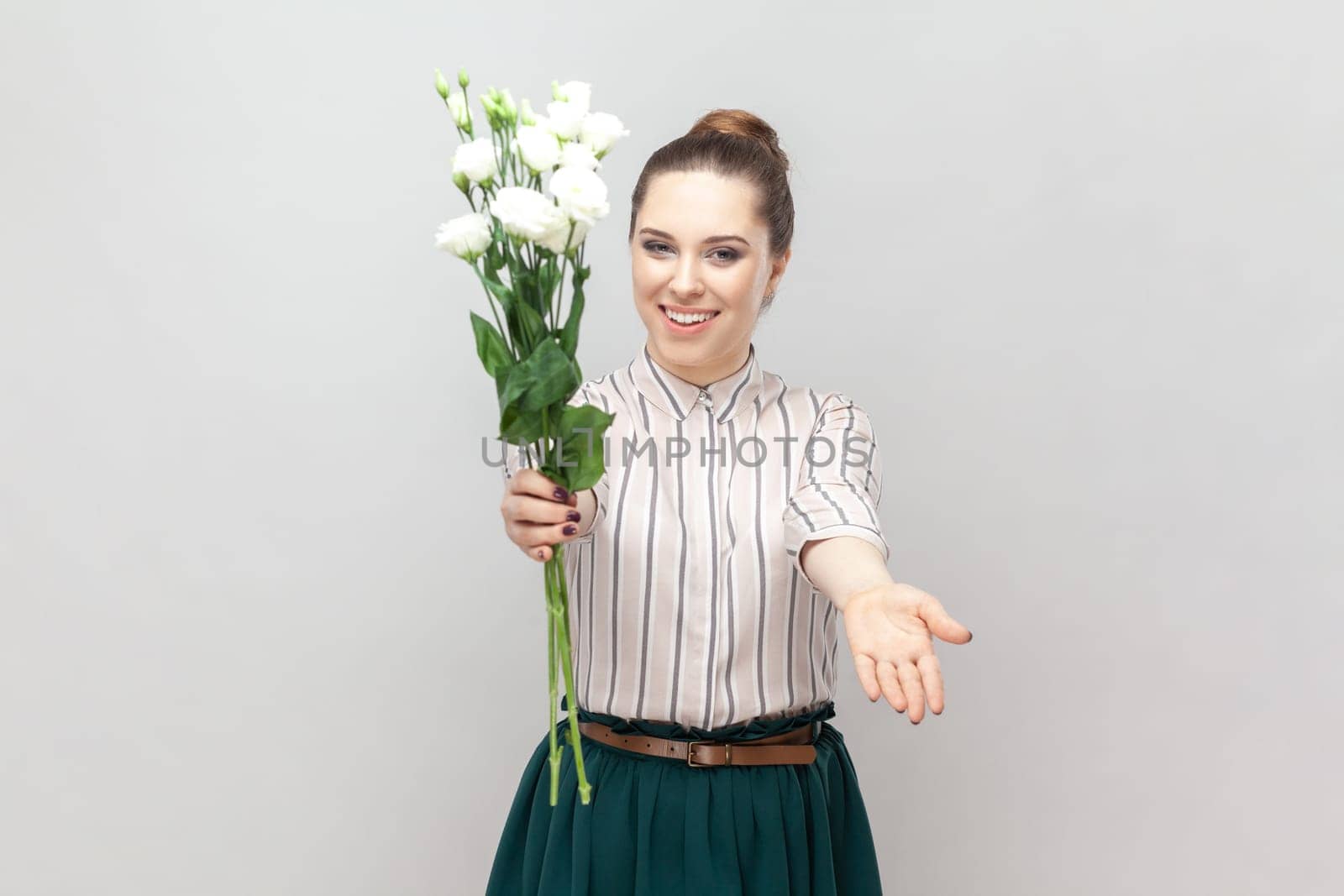Cheerful pretty woman holding bouquet of white flowers, spreading hand, giving it for you. by Khosro1