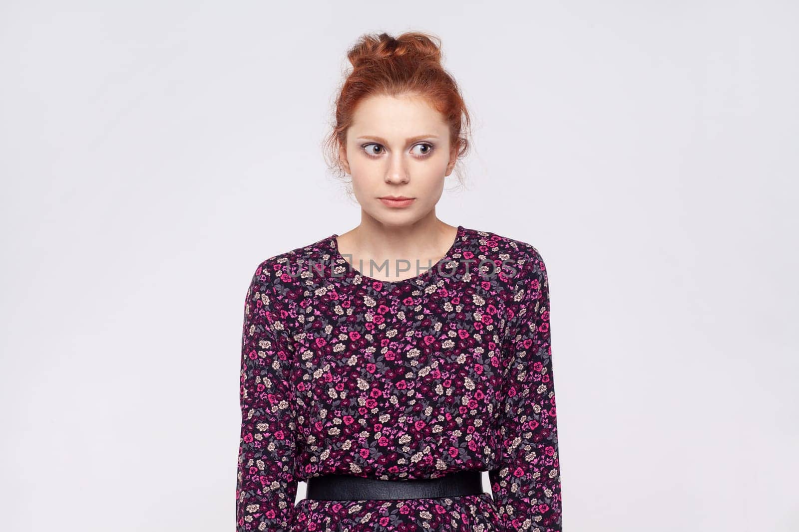 Portrait of worried serious young adult attractive ginger woman wearing dress looking away with scared, frighten expression, thinking. Indoor studio shot isolated on gray background.