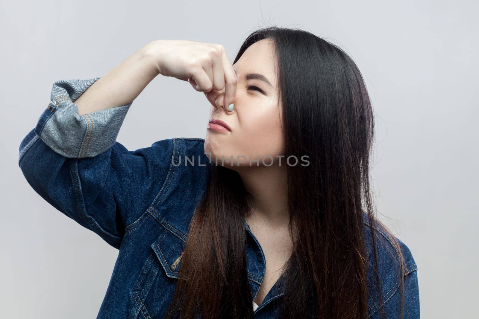 Disgusted brunette woman standing plugs nose as smells something stink and unpleasant feels aversion by Khosro1