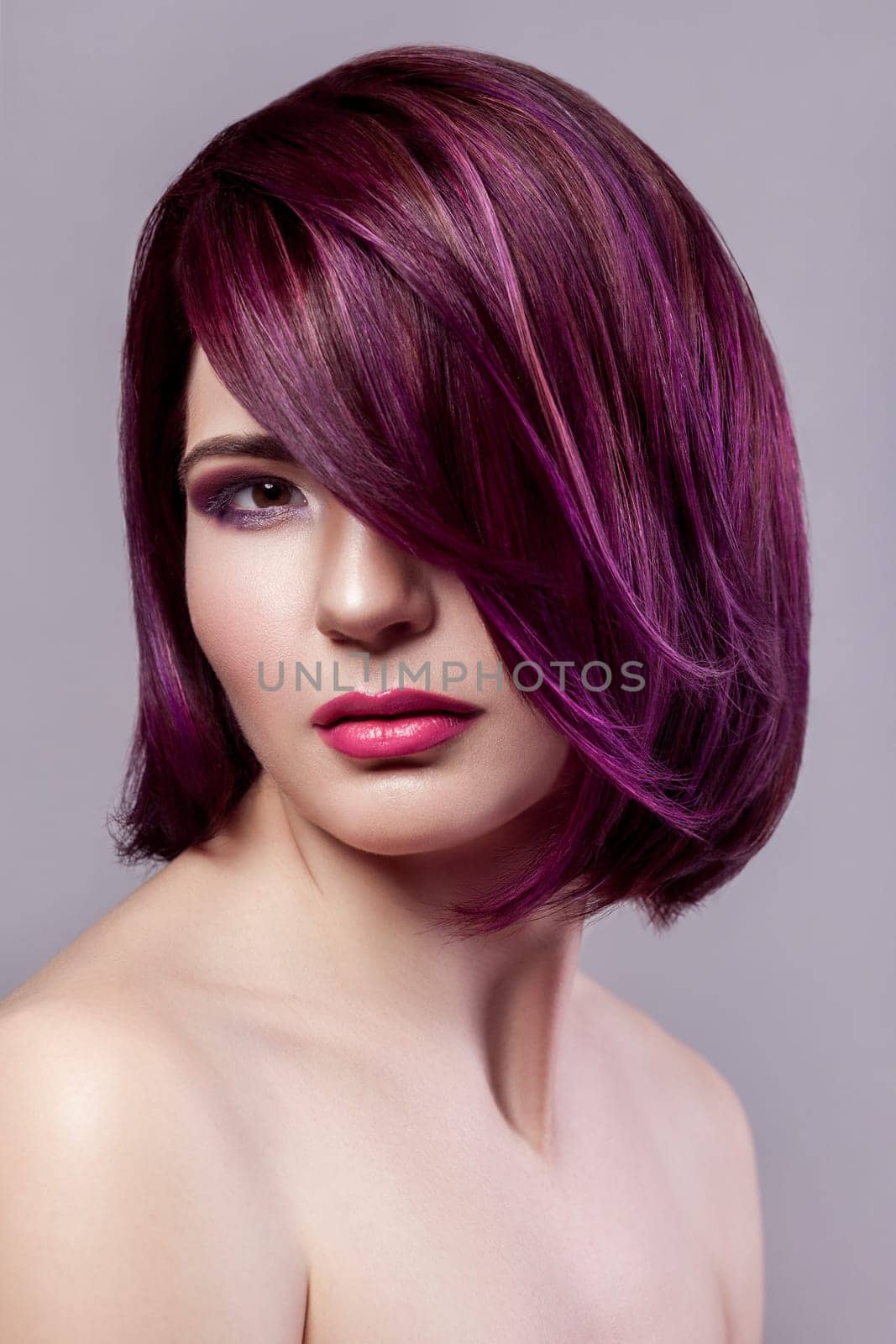 Beautiful woman with short purple colored hairstyle and makeup looks at camera with calm expression. by Khosro1