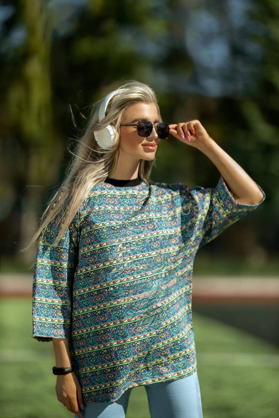 blonde athletic girl stands on the football field in a T-shirt, breeches, white sneakers and white headphones