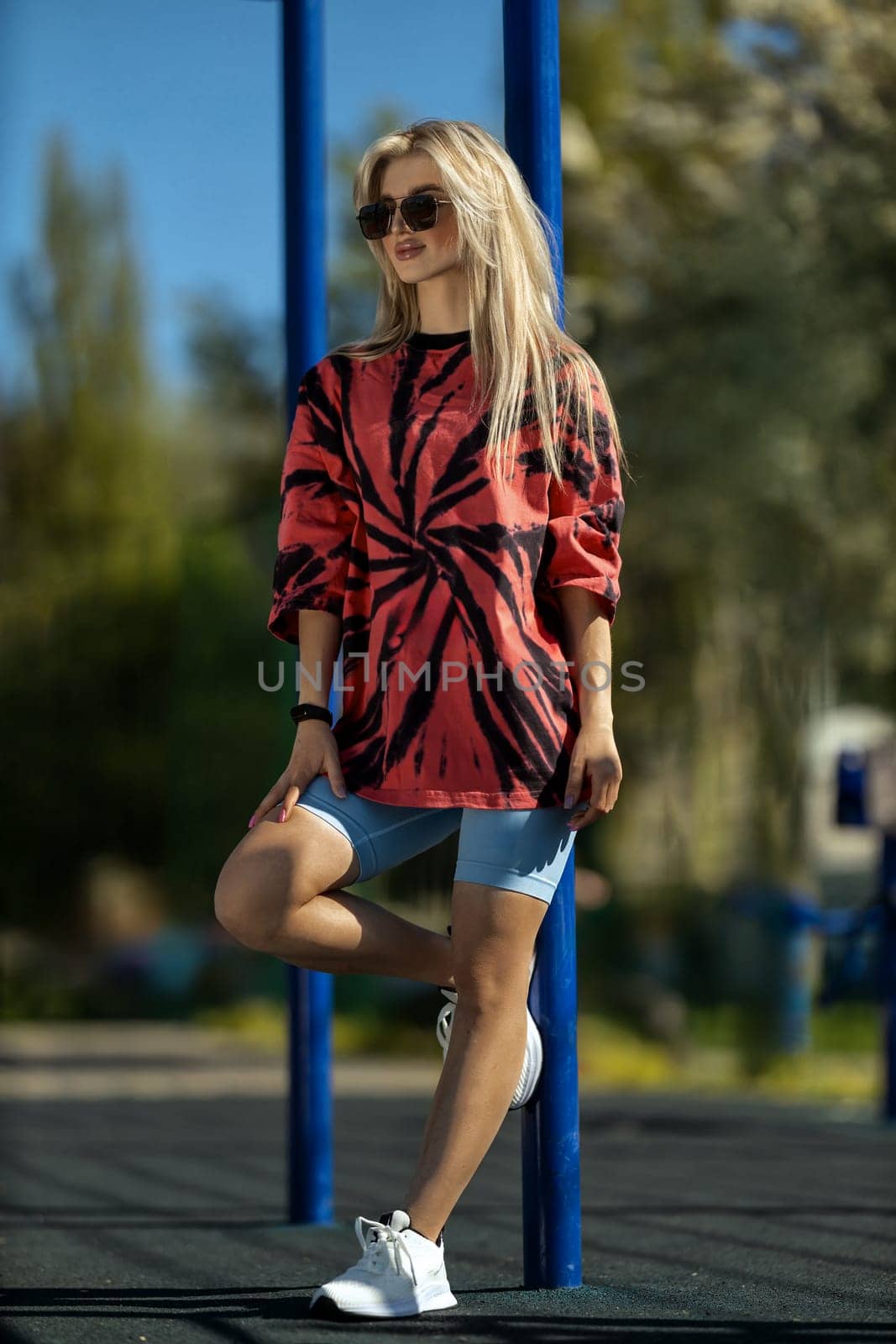 blonde athletic girl stands on the sports ground in a t-shirt, breeches, white sneakers and white headphones