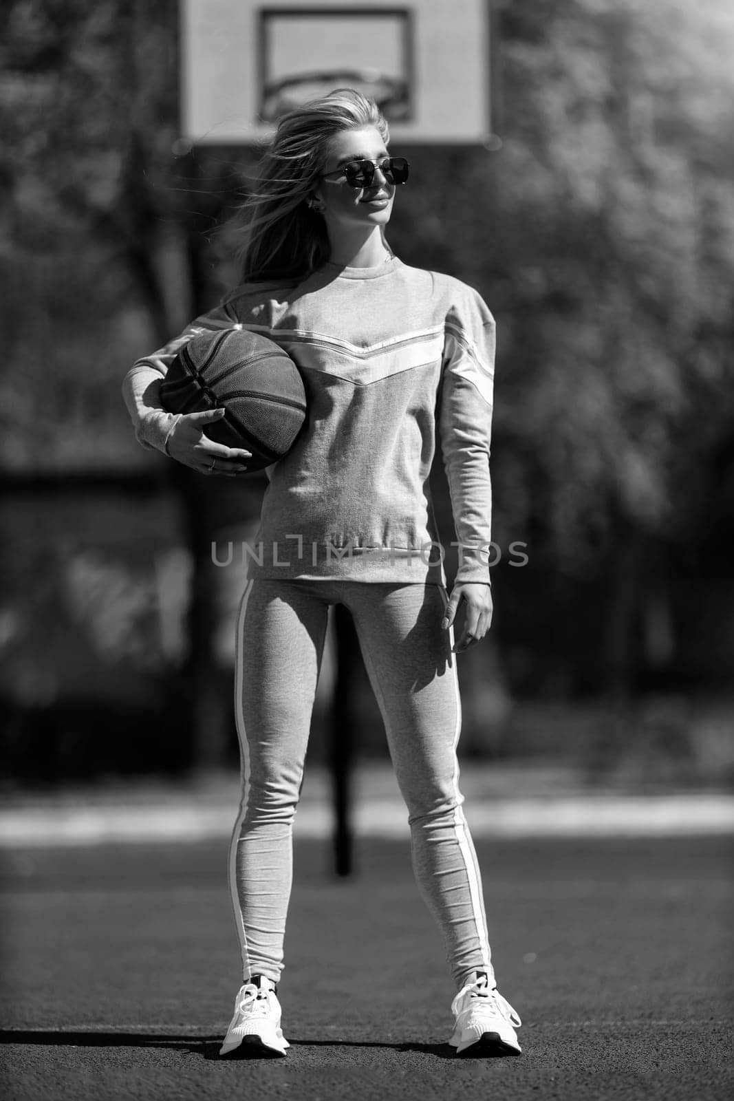 athletic blonde girl stands on the basketball court in a gray tracksuit with a ball in her hands black and white