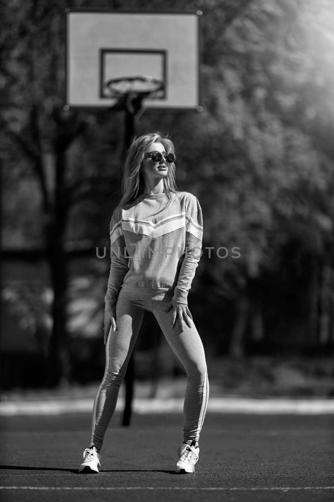 athletic blonde girl stands on the basketball court in a gray tracksuit black and white