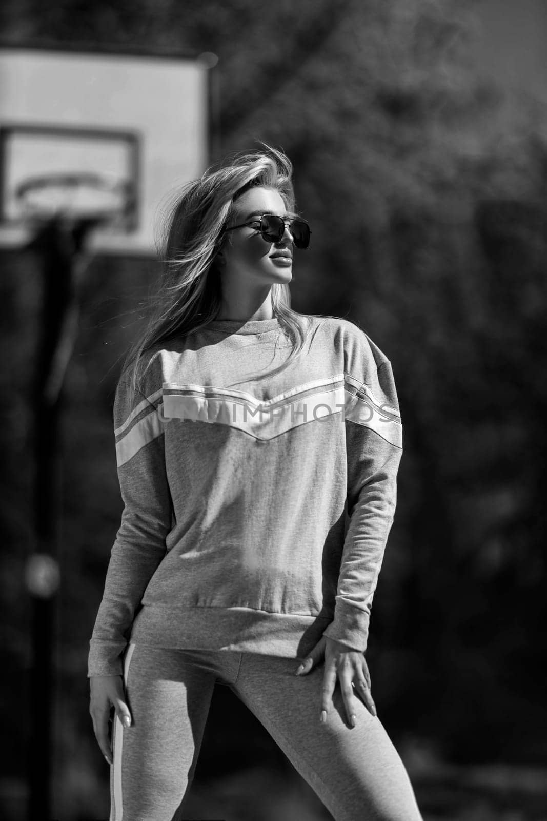 athletic blonde girl stands on the basketball court in a gray tracksuit black and white