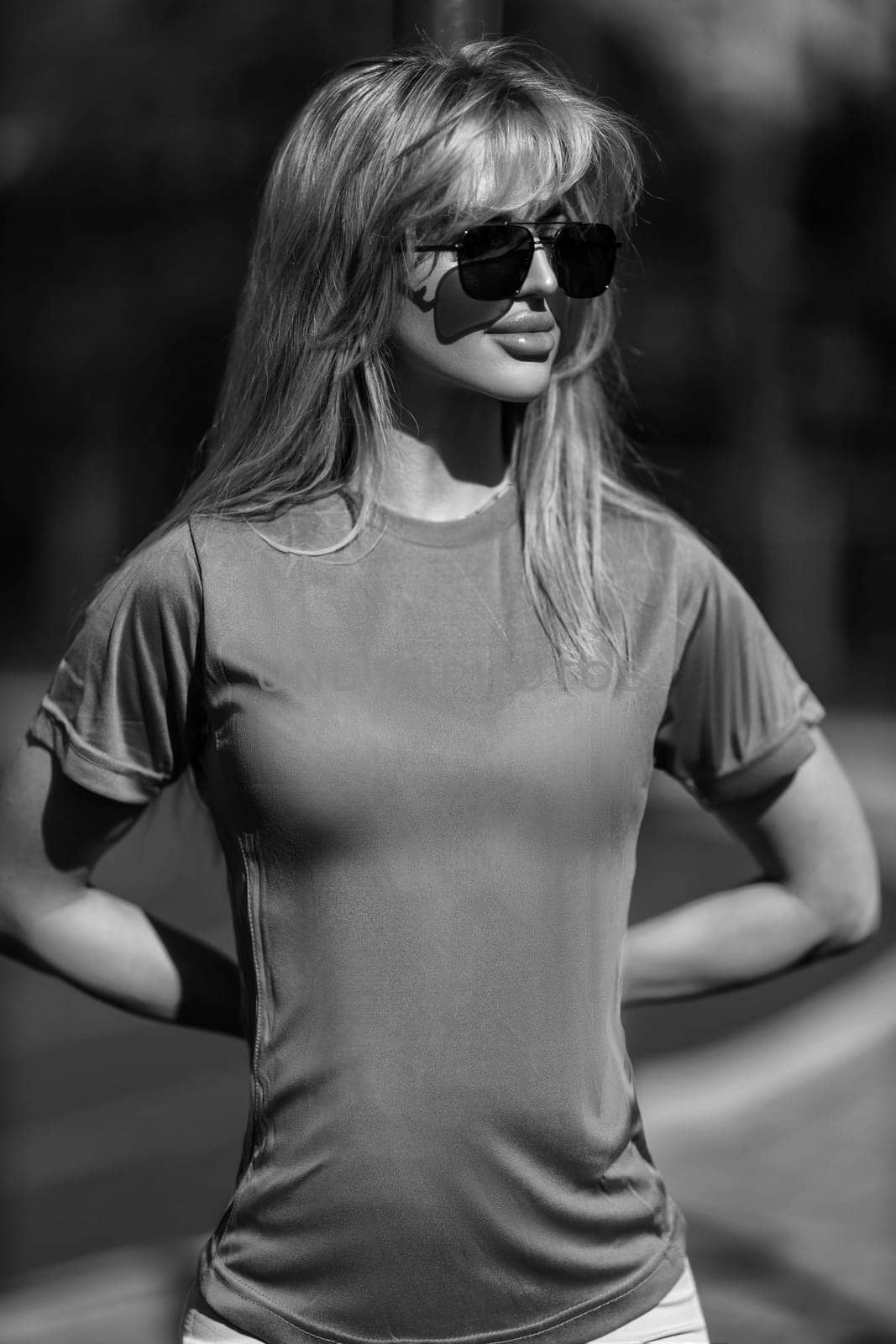 blonde athletic girl stands on the sports ground in a t-shirt, breeches, white sneakers and white headphones black and white