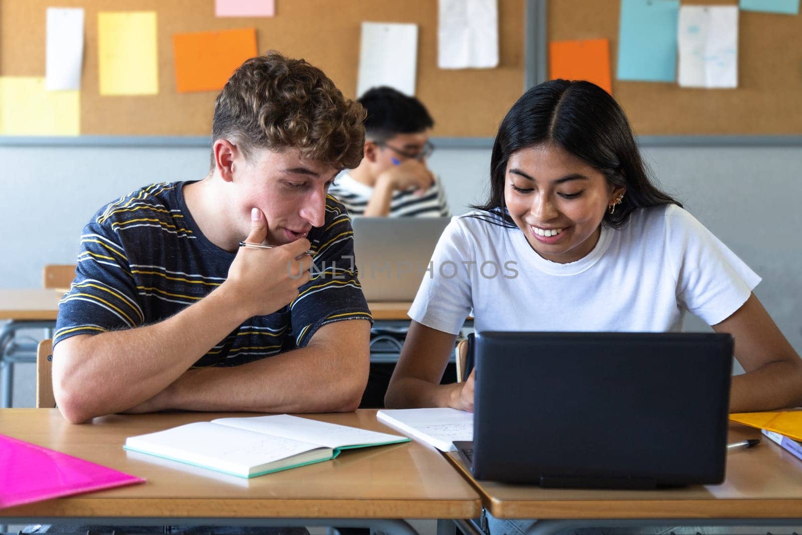 Caucasian teen boy and native american teenage female high school students in class working together on school project using laptop. Education concept.