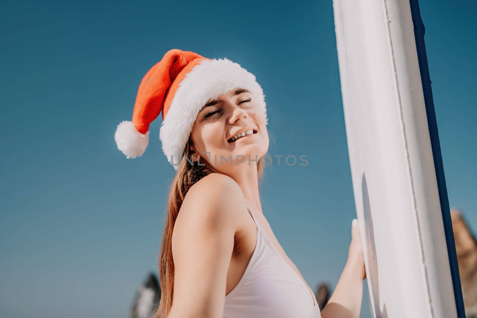 Woman sea sup. Close up portrait of happy young caucasian woman with long hair in Santa hat looking at camera and smiling. Cute woman portrait in a white bikini posing on sup board in the sea by panophotograph