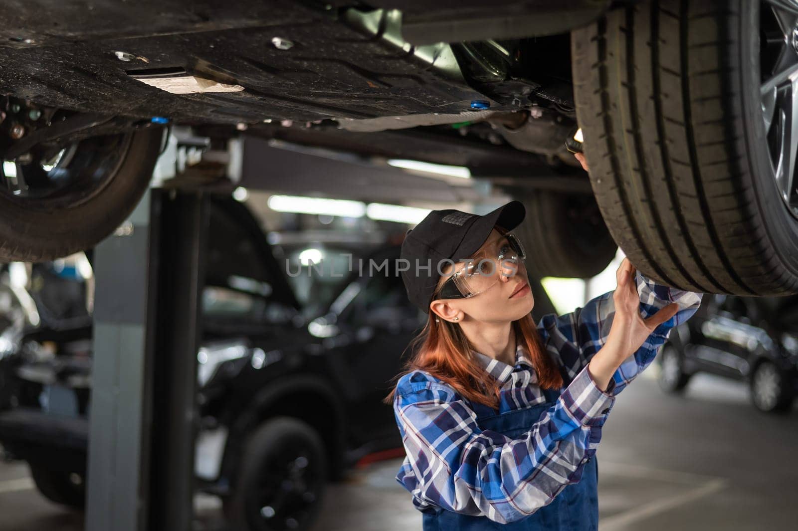 A female mechanic inspects a lifted car. A girl at a man's work