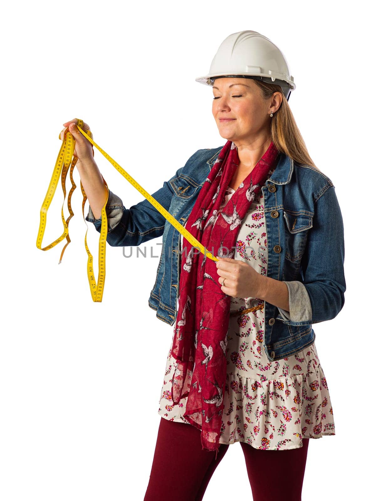 Forty year old woman, wearing bohemian style clothing and a hard har, holding a yellow mesuring tape, isolated on a white background