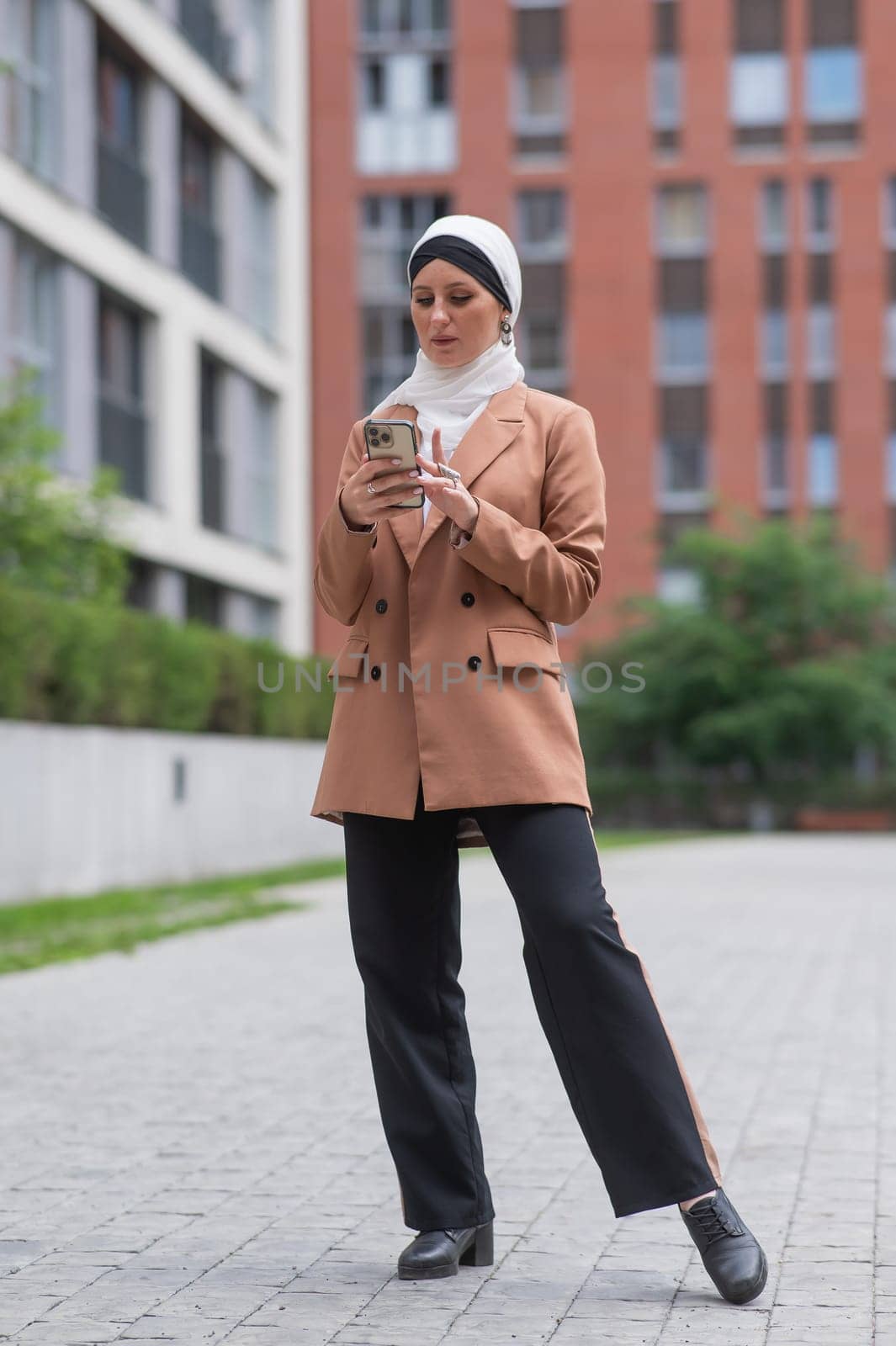 Young woman in hijab using smartphone outdoors