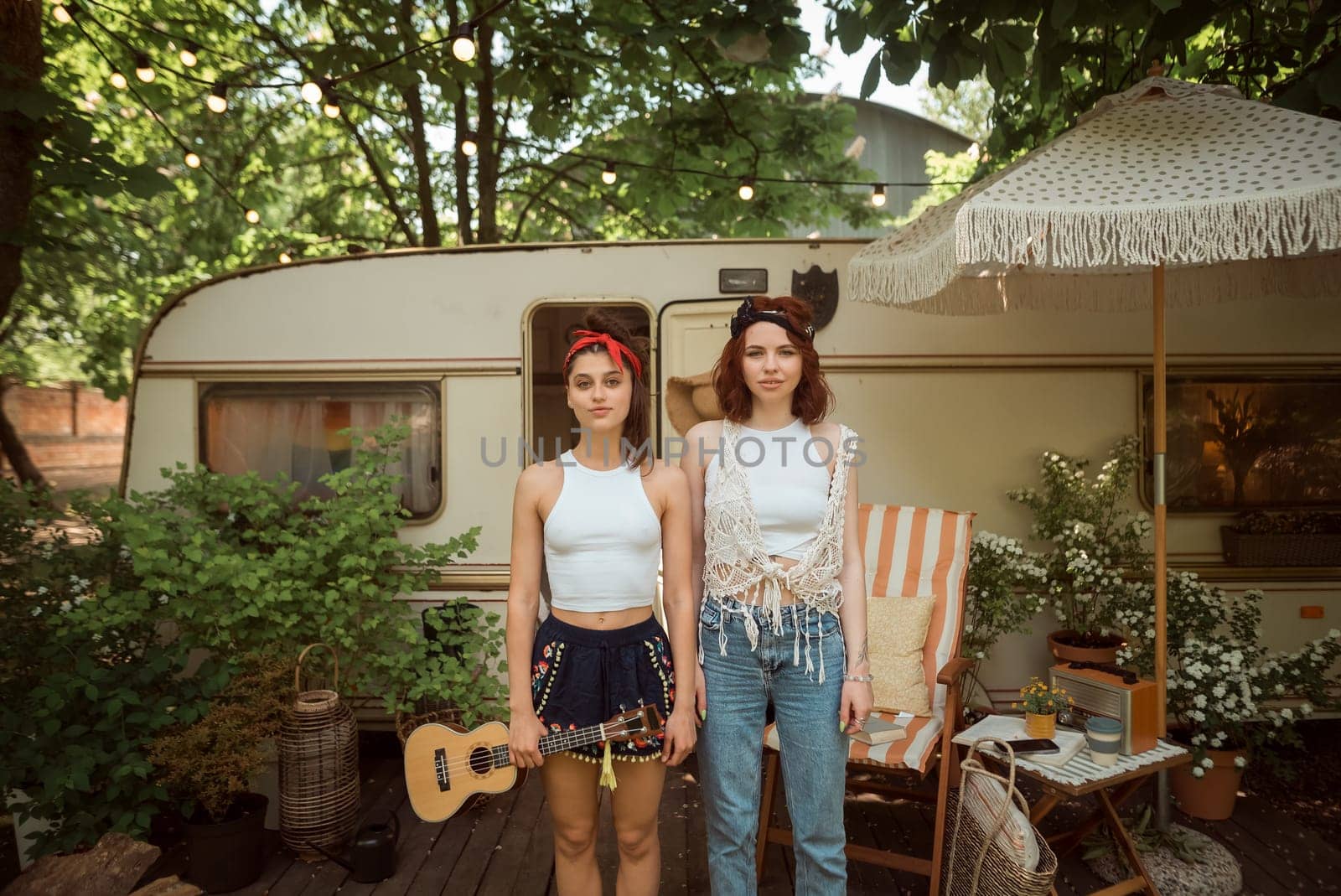 Happy hippie girls are having a good time with playing on guitar in camper trailer. Holiday, vacation, trip concept.High quality photo