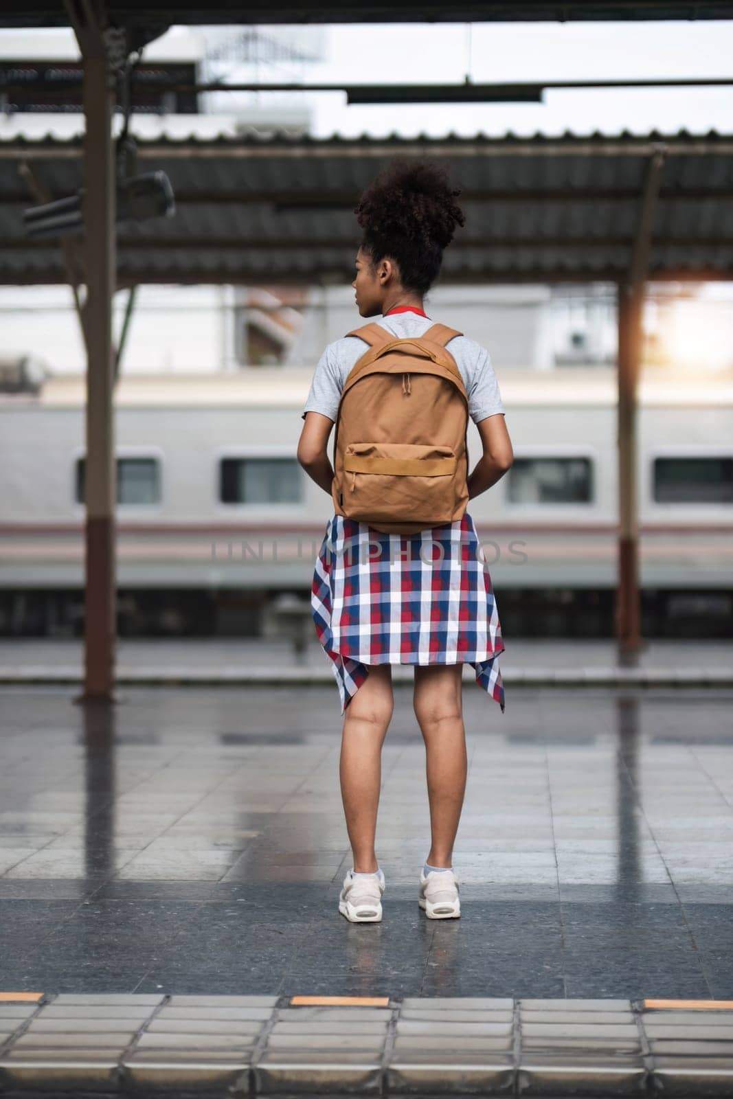Young Asian African woman traveler with backpack in the railway train station, traveler girl walking stand sit waiting take a picture on railway platform train station. High quality photo..