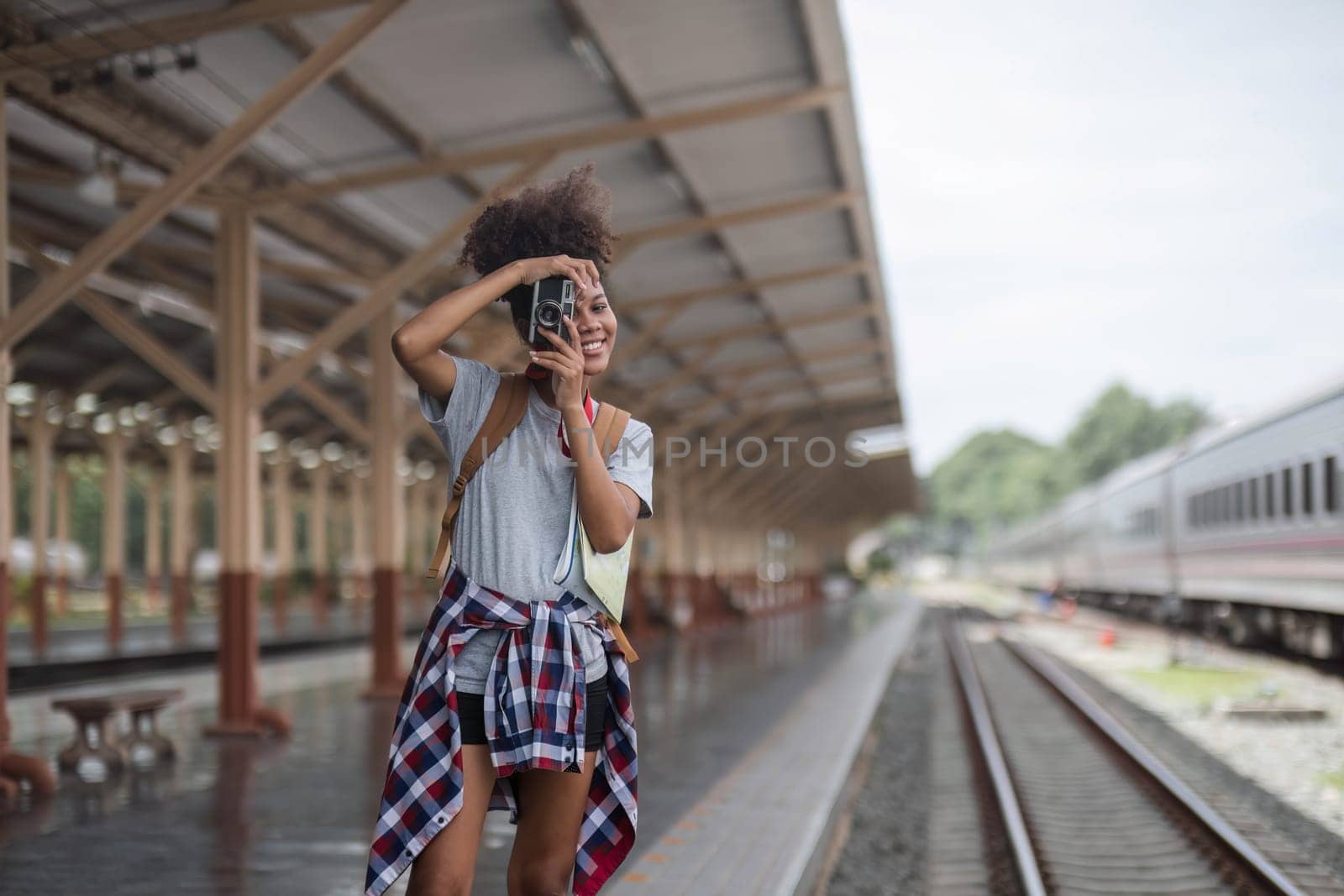 Young Asian African woman traveler with backpack in the railway train station, traveler girl walking stand sit waiting take a picture on railway platform train station. High quality photo by wichayada