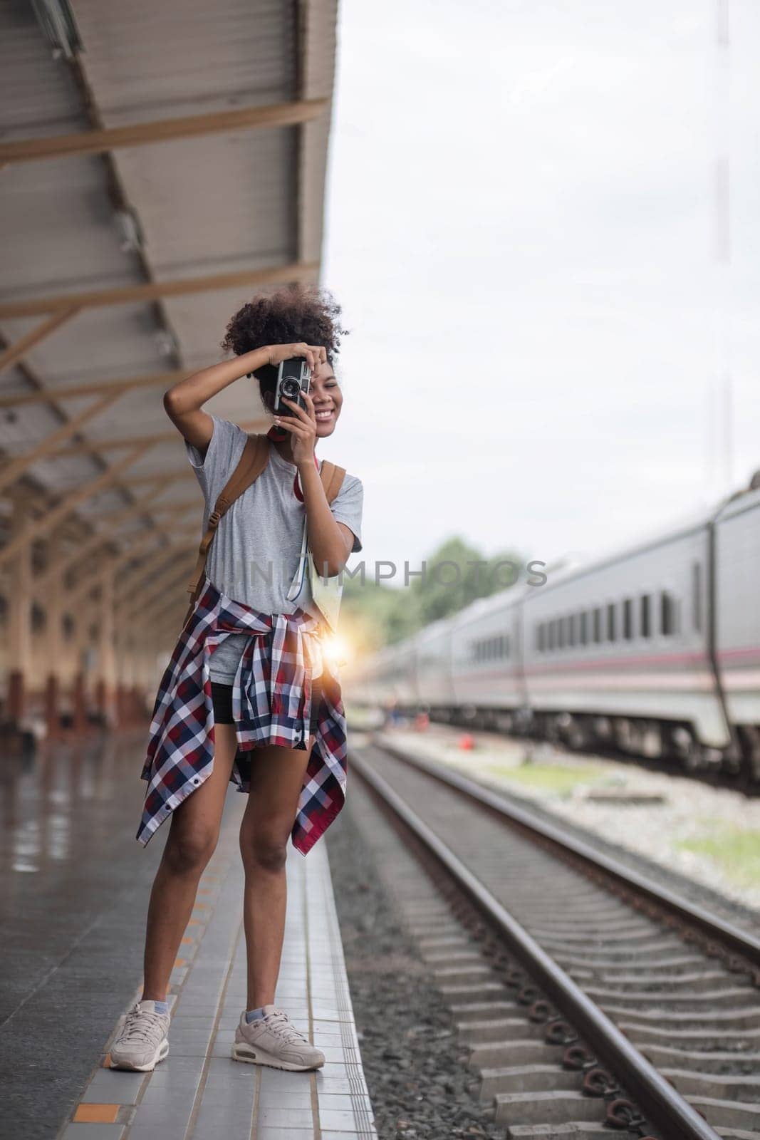 Young Asian African woman traveler with backpack in the railway train station, traveler girl walking stand sit waiting take a picture on railway platform train station. High quality photo by wichayada