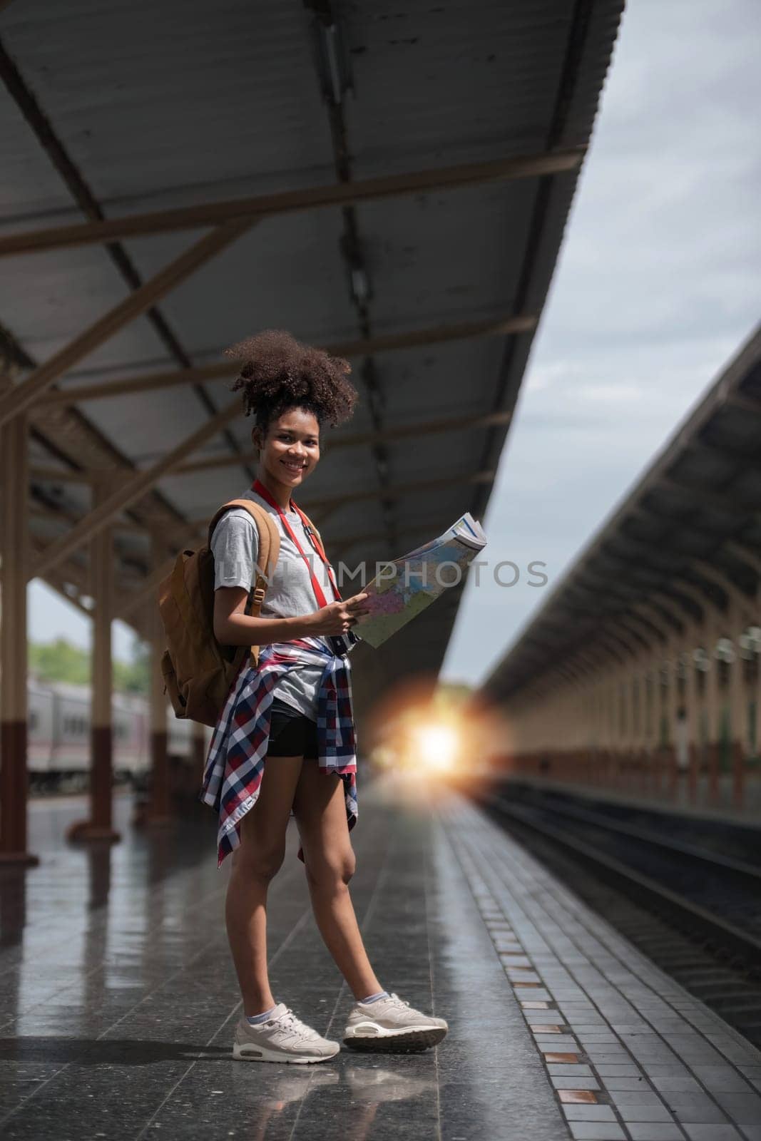 Young woman female smiling traveler with back pack looking to map while waiting for the train at train station. High quality photo..