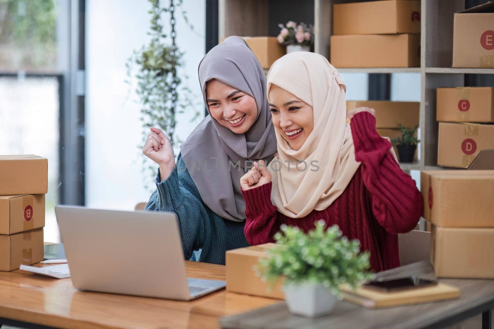 Two women muslim look at online product sales data on laptops and show joy..