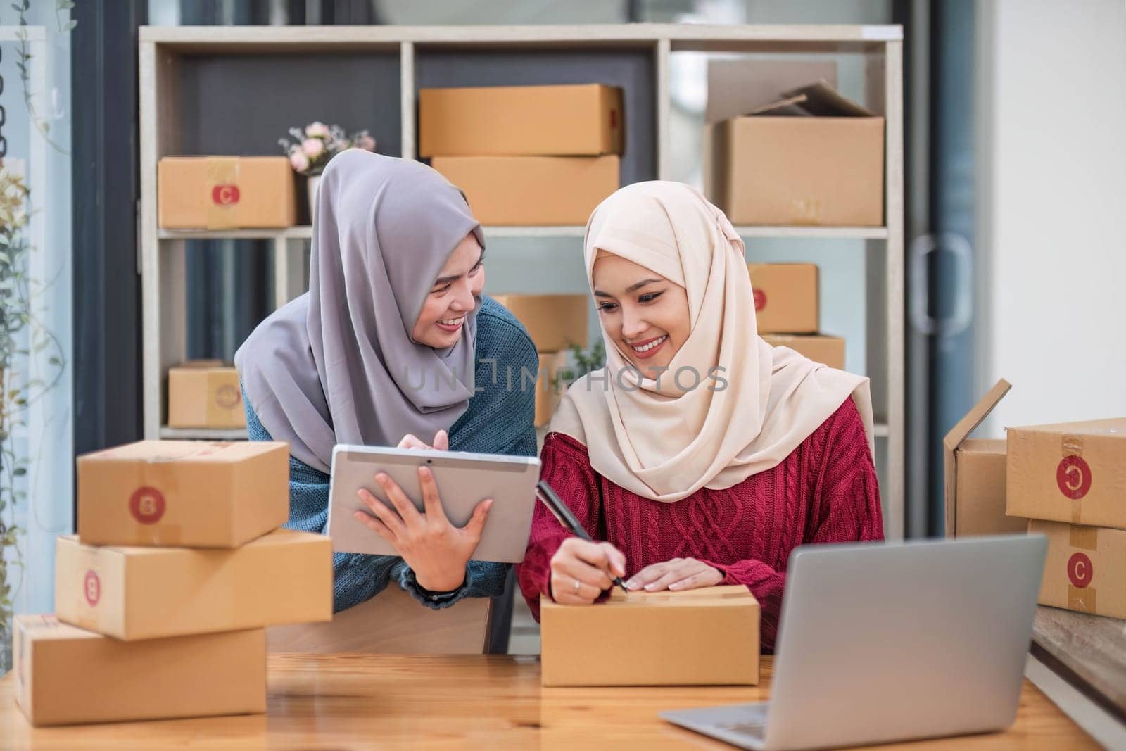 Friend muslim female work independent business sme online shopping working on laptop computer with parcel box on desk at home, SME online business and delivery concept..