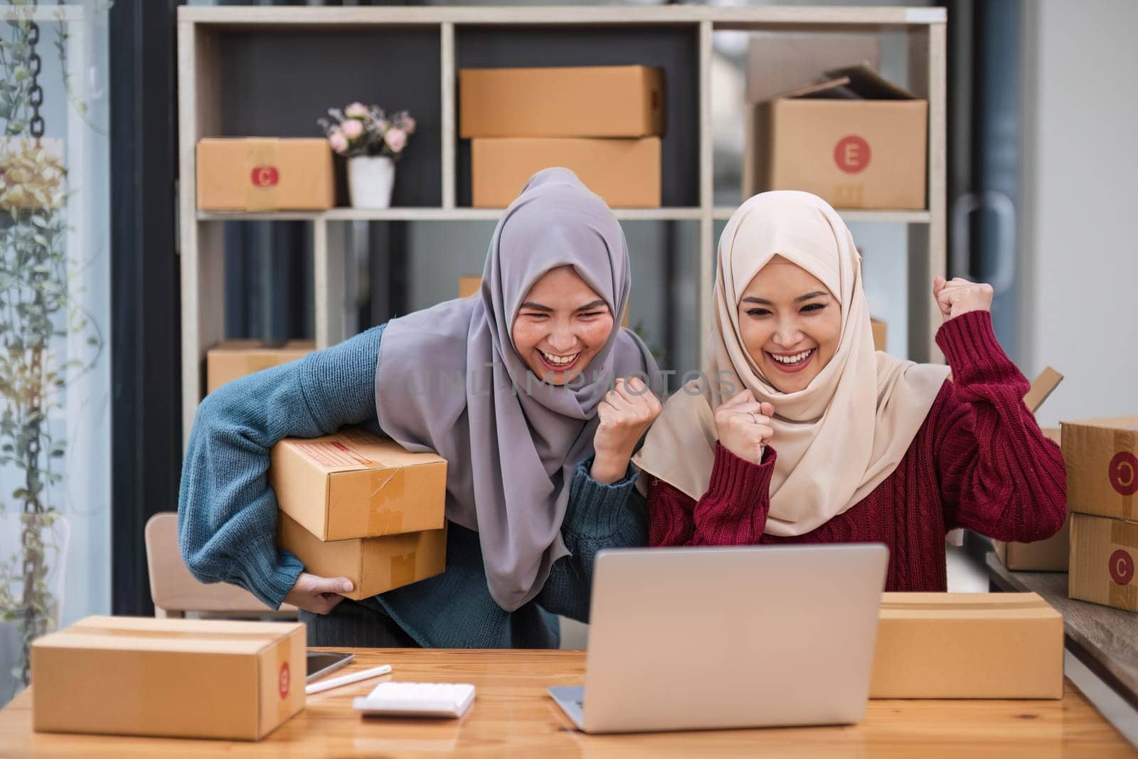 Two women muslim look at online product sales data on laptops and show joy..