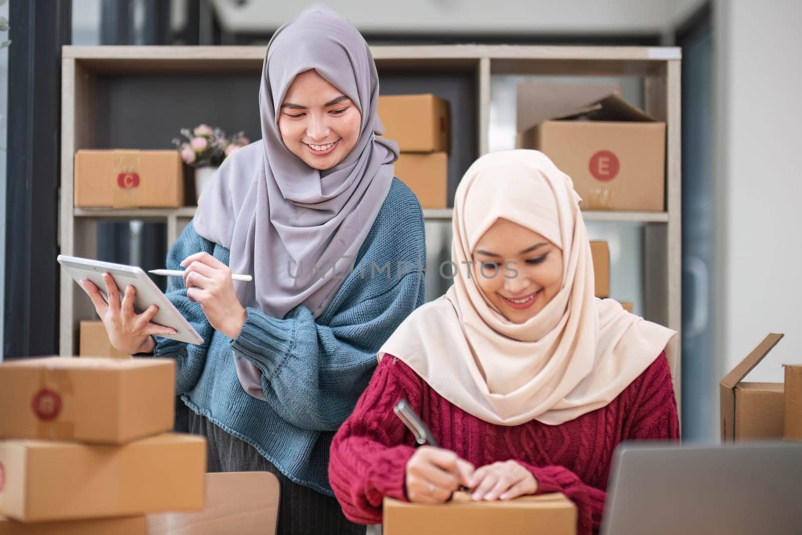 Friend muslim female work independent business sme online shopping working on laptop computer with parcel box on desk at home, SME online business and delivery concept..