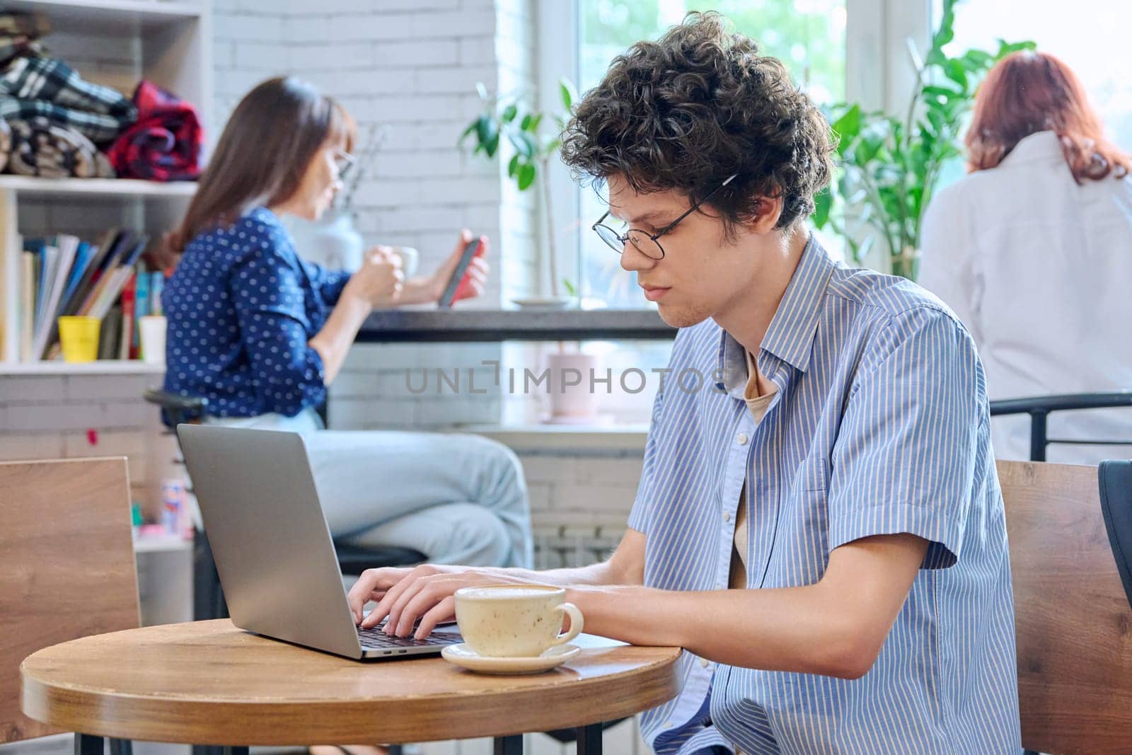 Guy college student typing on laptop, sitting at table in coffee shop with cup of coffee. by VH-studio