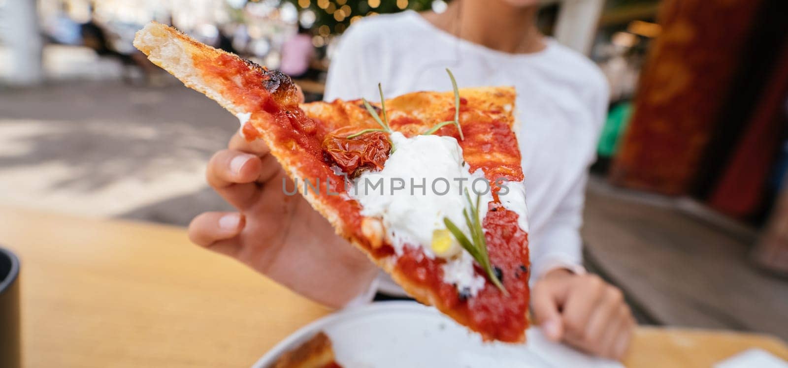 Woman's hand holding a slice of pizza outdoor on terrace.