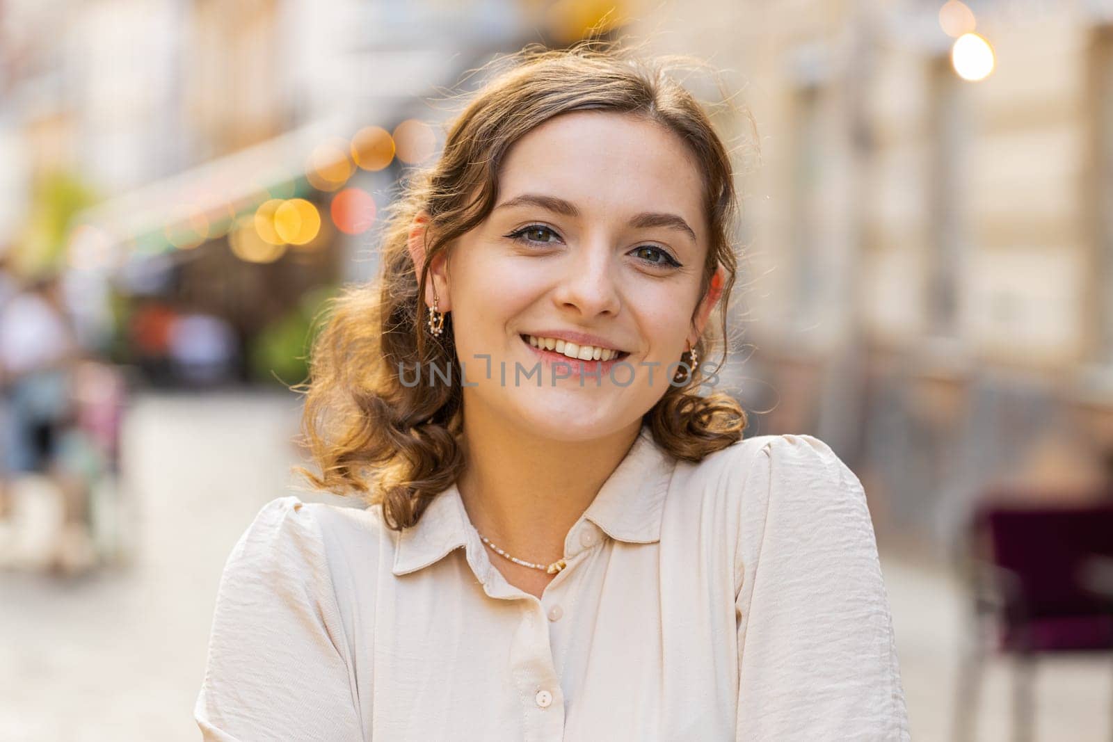 Portrait of happy pretty young woman smiling friendly, glad expression looking at camera dreaming, resting, relaxation feel satisfied good news outdoors. Girl in urban city sunshine street background