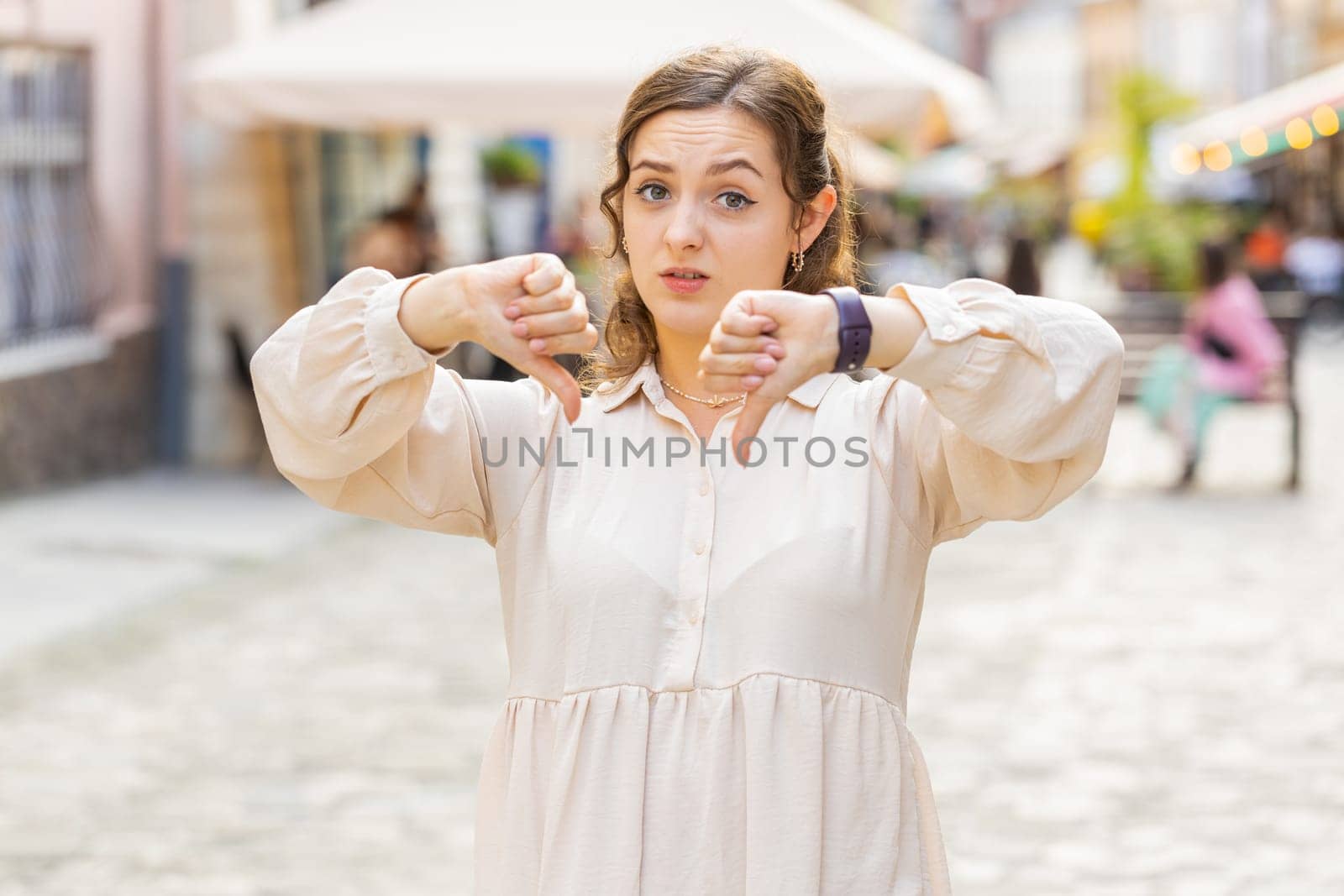Dislike. Upset young pretty woman showing thumbs down sign gesture, expressing discontent, disapproval, dissatisfied bad work, mistake. Displeased lovely girl walking in urban city street outdoors