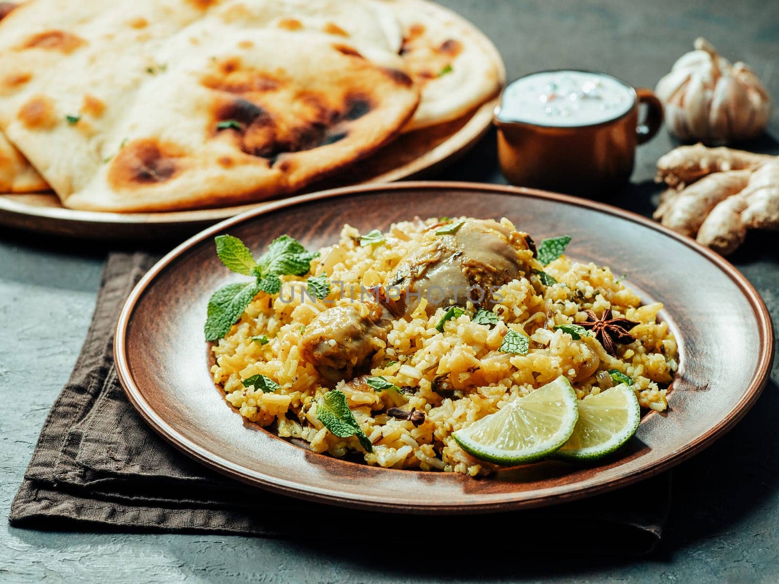 Pakistani food - biryani rice with chicken, raita yoghurt dip and naan flat bread. Delicious hyberabadi chicken biryani on black background
