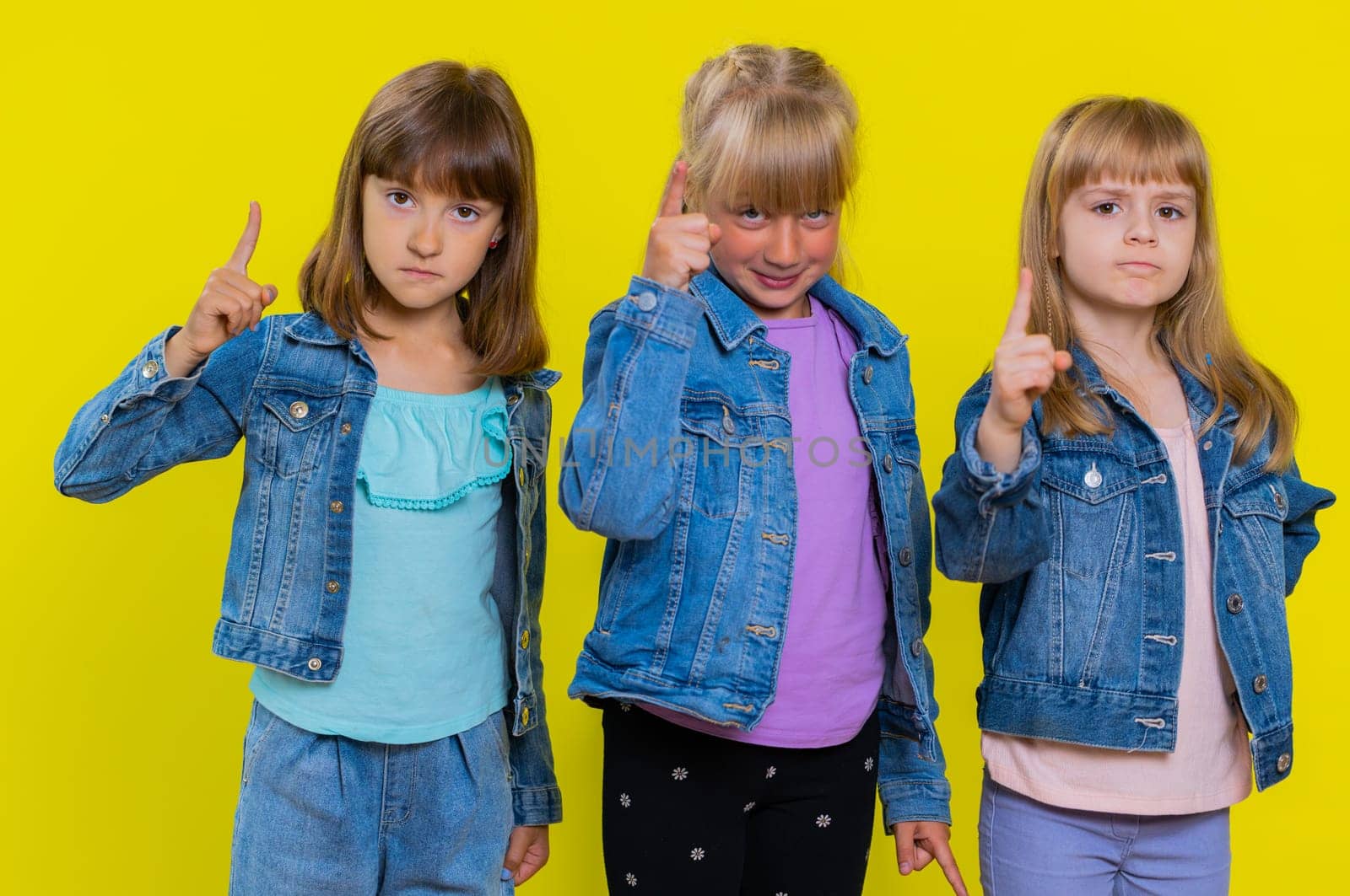 Quarrel. Displeased teenage girls gesturing hands with irritation and displeasure, blaming scolding for failure, asking why this happened. Children sisters. Three siblings kids on yellow background