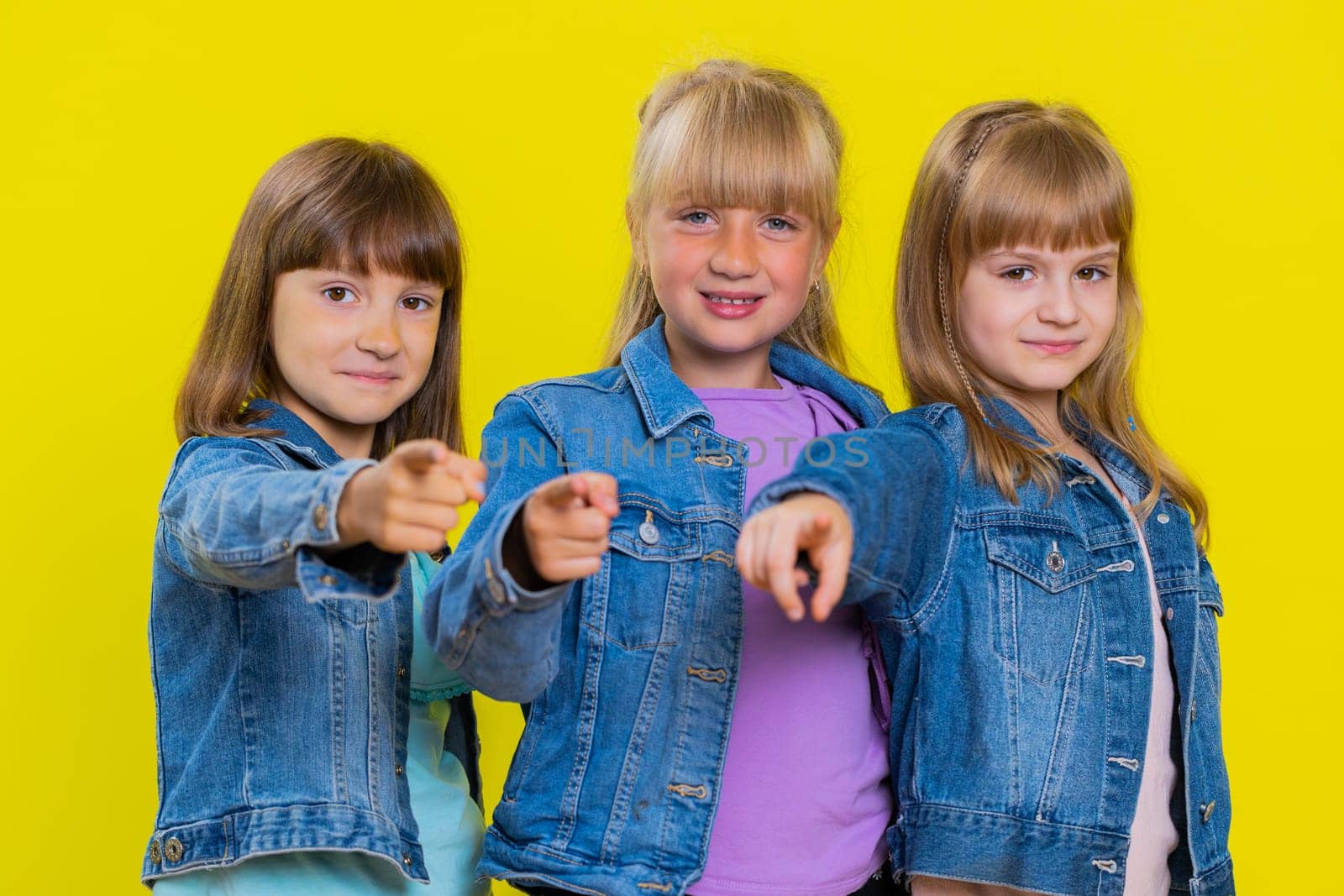 Hey you. Teenage girls smiling excitedly and pointing to camera, choosing lucky winner indicating to awesome you. Little children sisters. Three cute siblings kids isolated on studio yellow background