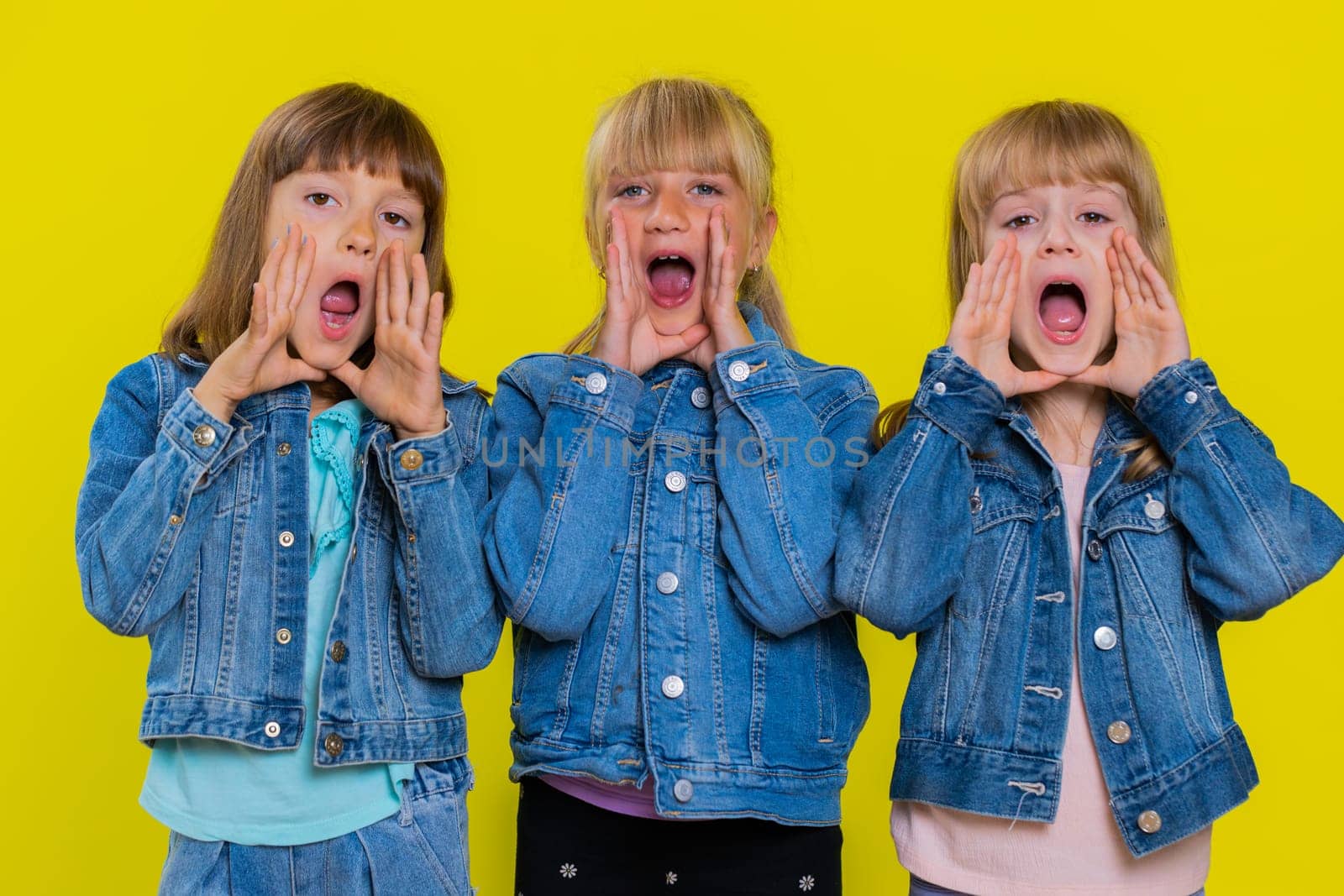 Expressive teenage girls holding hands near mouth loudly screaming, shouting, yelling, announces discounts sale Hurry up, welcomes someone hello. Little children sisters. Three female siblings kids