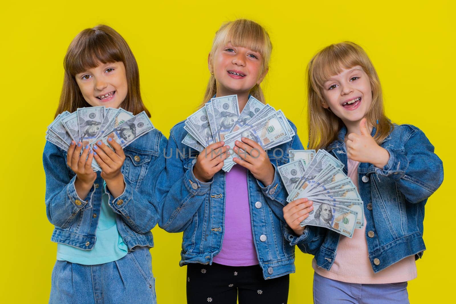 Rich happy teenage girls waving money dollar cash banknotes bills like a fan, success business career, lottery game winner, big income, wealth, donation. Little children sisters. Three siblings kids