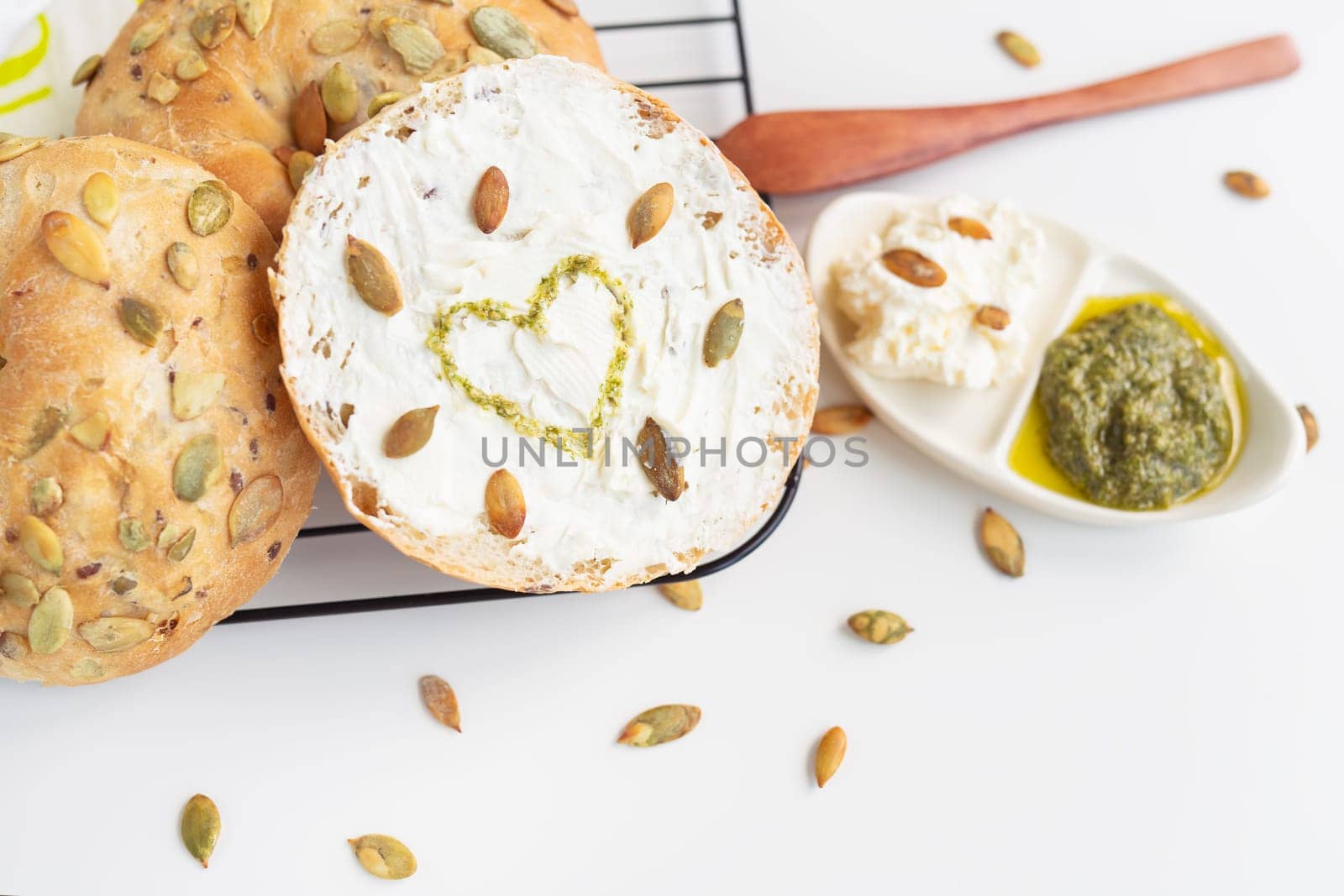 Freshly baked bagel with Philadelphia cheese, sunflower seeds and a painted heart with pesto sauce. Delicious and healthy breakfast
