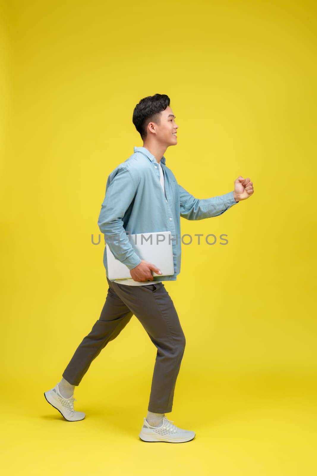 young man happy positive smile go walk hold laptop meeting isolated over yellow color background