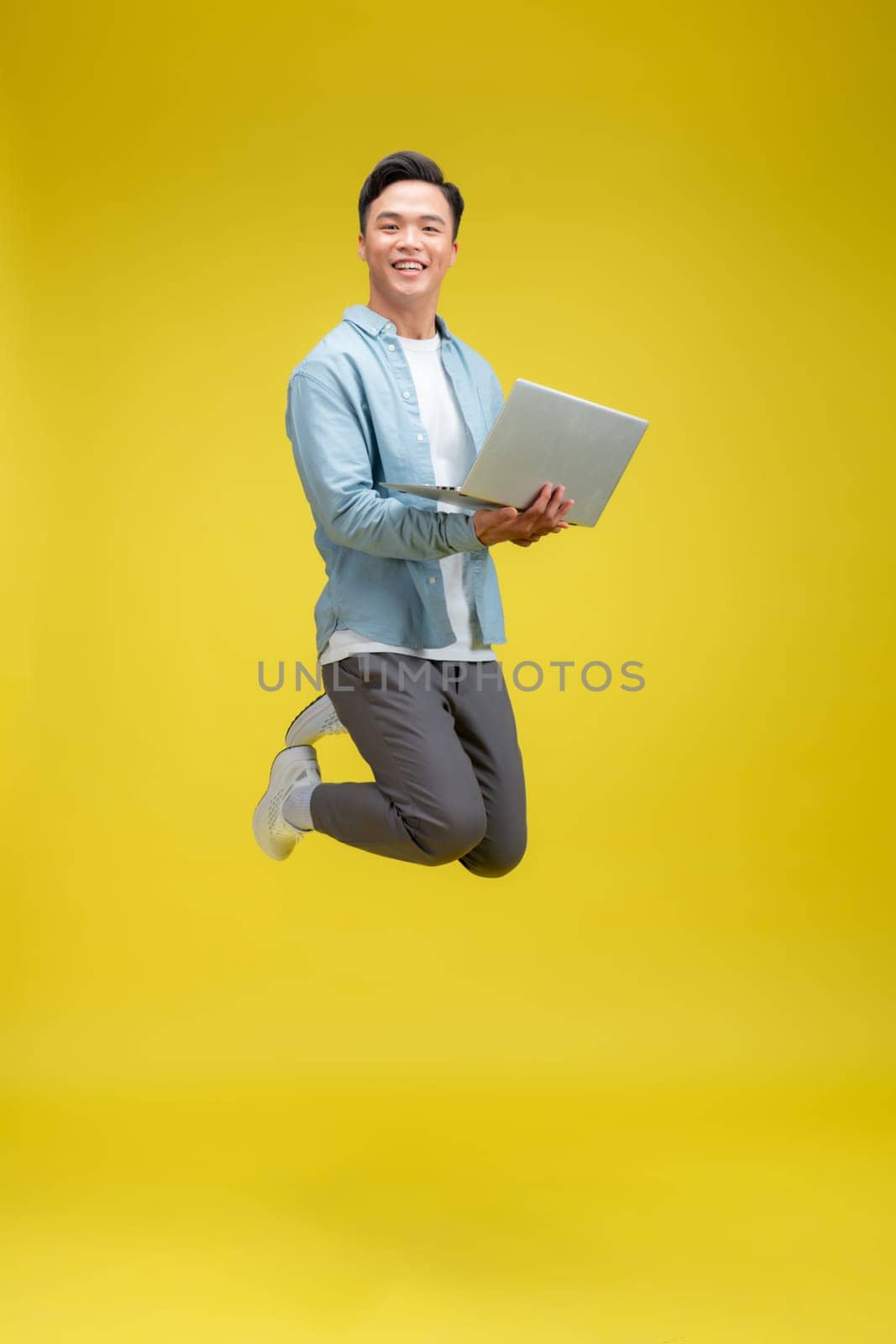 happy excited young african man jumping isolated over yellow background using laptop computer.