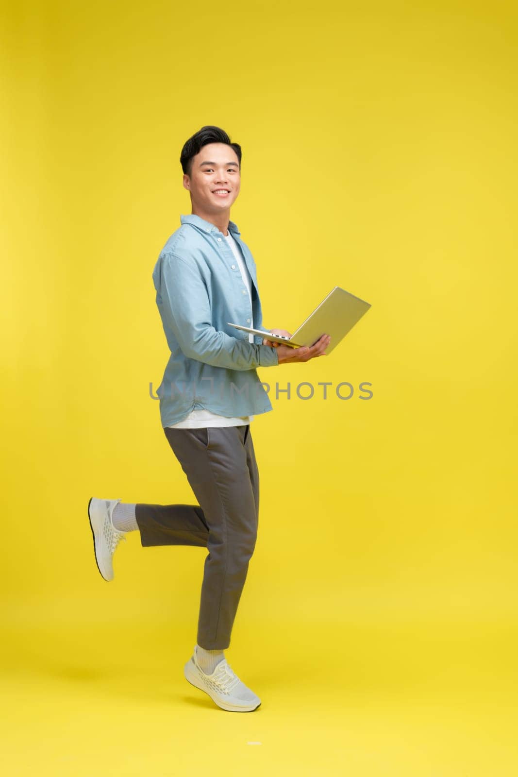 happy excited young african man jumping isolated over yellow background using laptop computer.