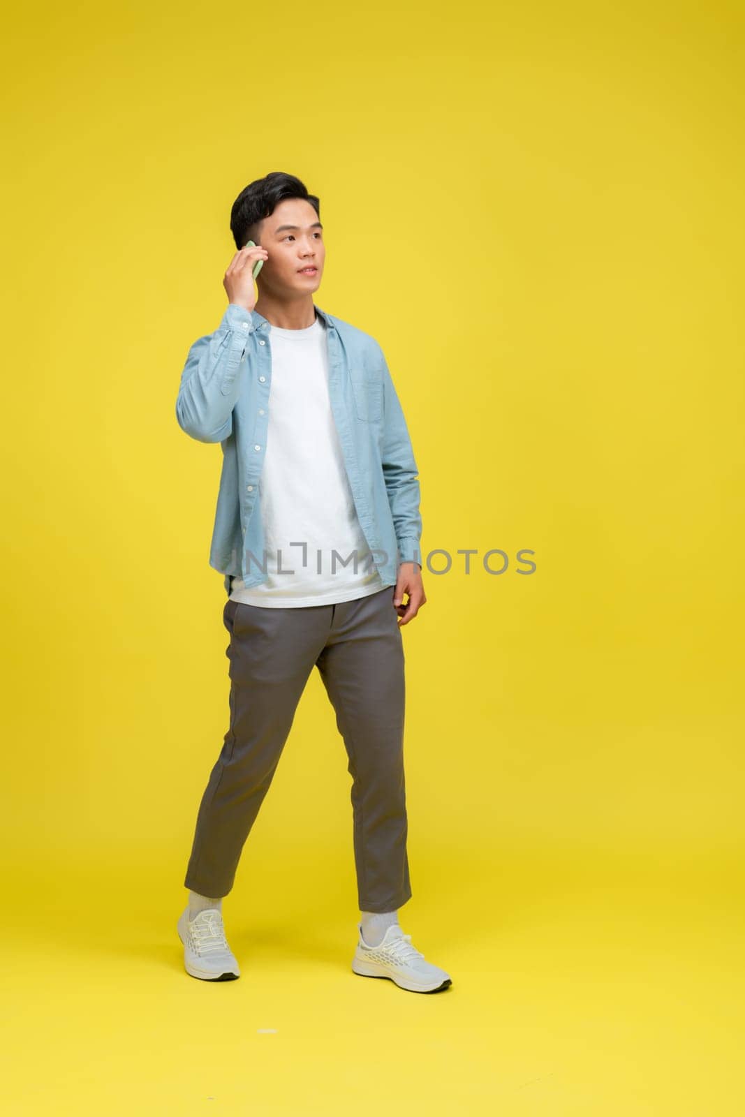 Full length shot of man walking and using talk smartphone isolated on yellow background.