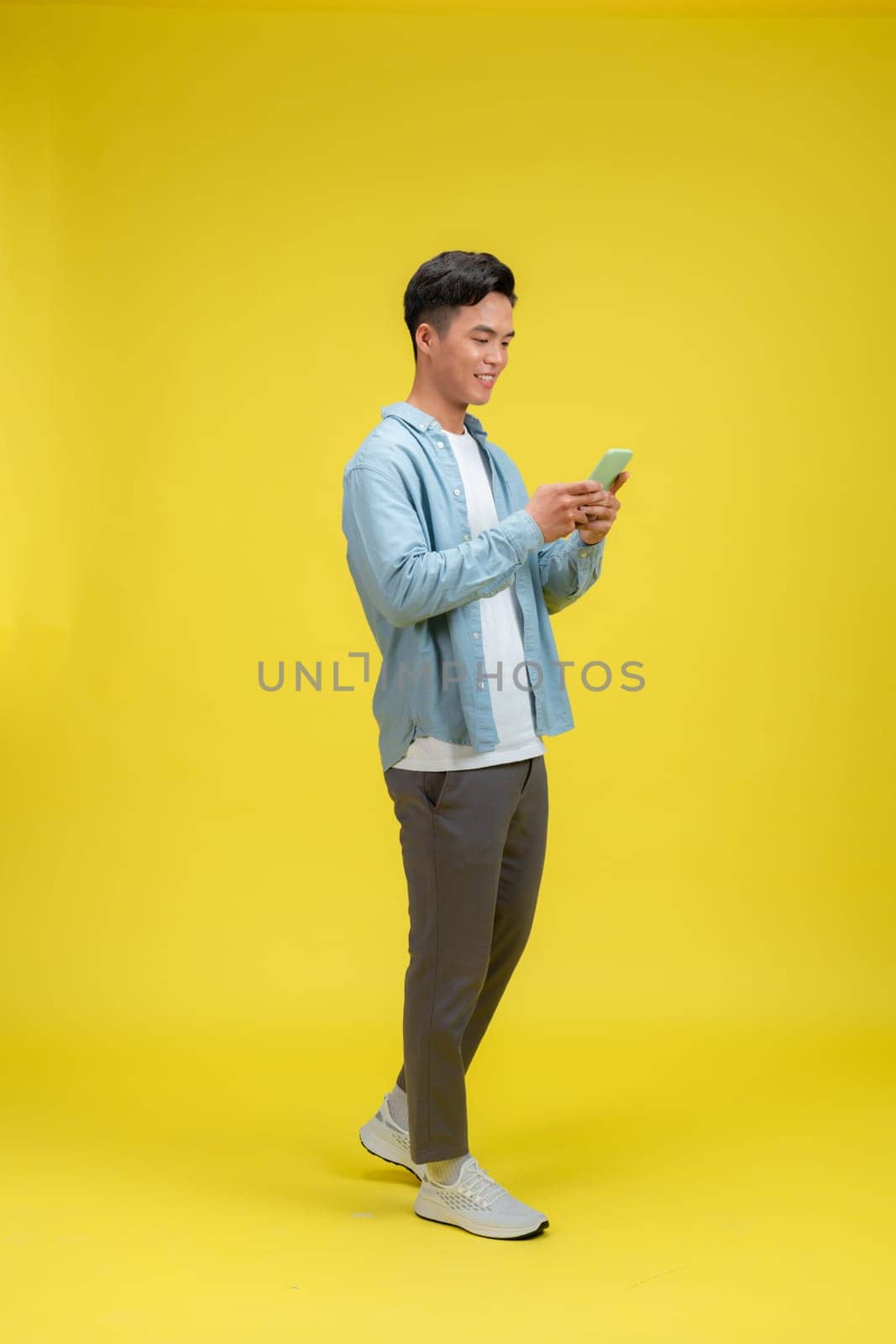 Cheerful young man using smartphone while looking at screen and walking