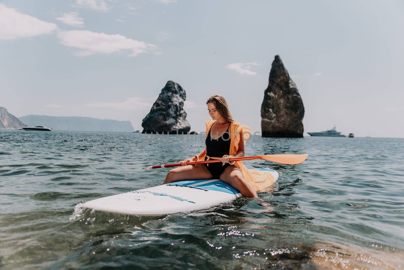 Close up shot of beautiful young caucasian woman with black hair and freckles looking at camera and smiling. Cute woman portrait in a pink bikini posing on a volcanic rock high above the sea