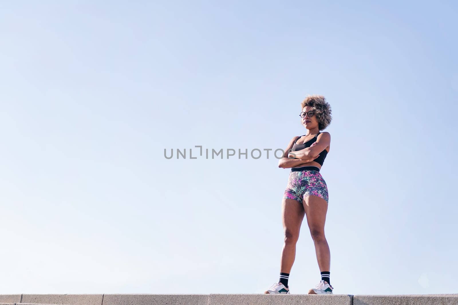low angle view portrait of an african american strong woman with sportswear standing outdoors with arms crossed, concept of sports and active lifestyle, copy space for text