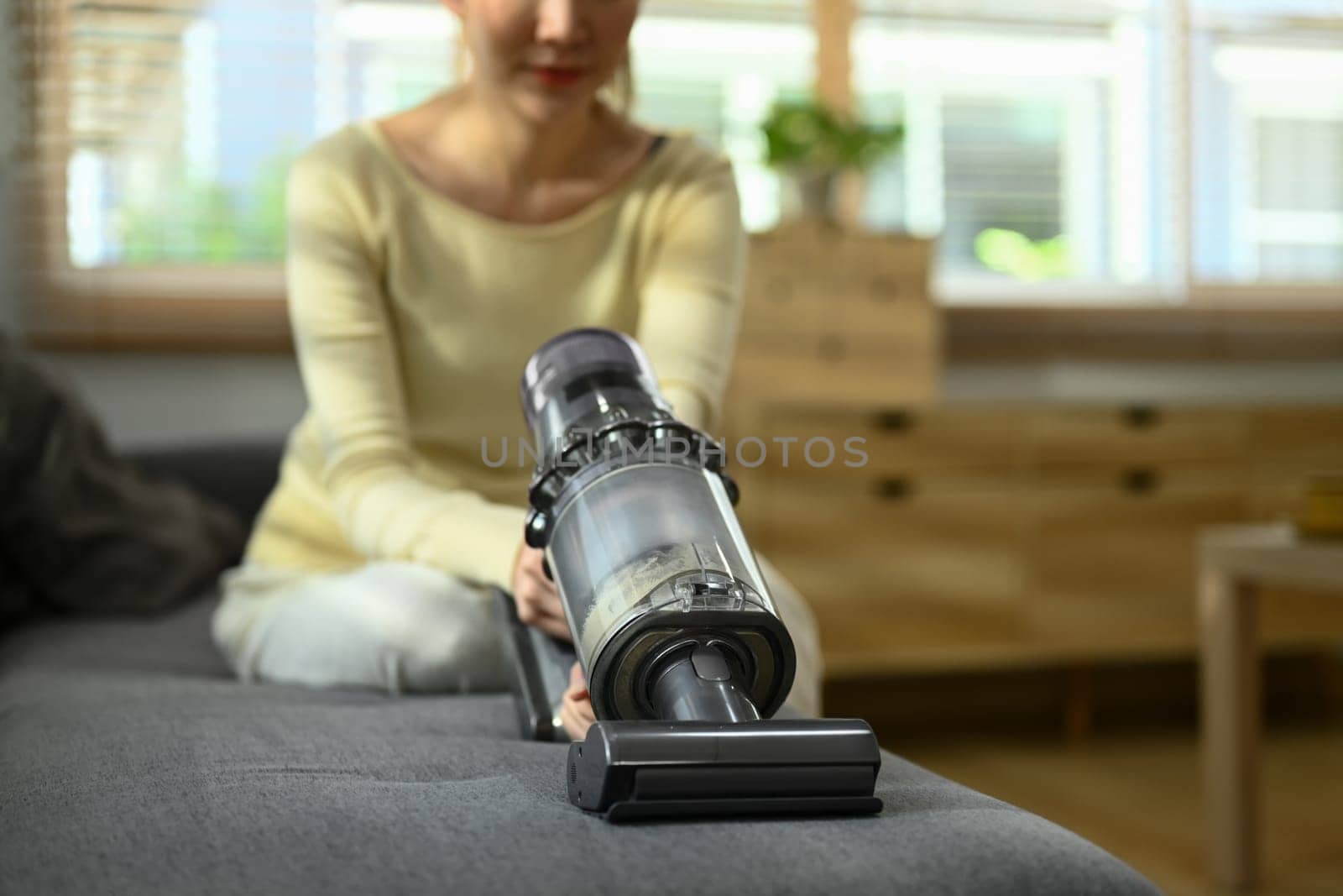 Woman vacuuming germs and dirt on couch in living room. House cleaning and housework concept.