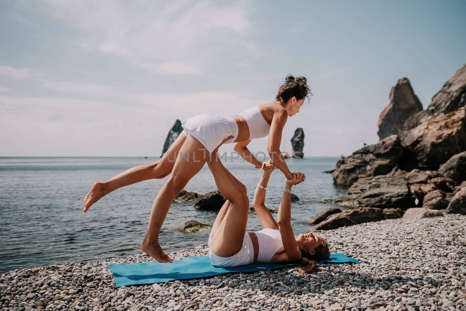 Woman sea yoga. Two Happy women meditating in yoga pose on the beach, ocean and rock mountains. Motivation and inspirational fit and exercising. Healthy lifestyle outdoors in nature, fitness concept. by panophotograph